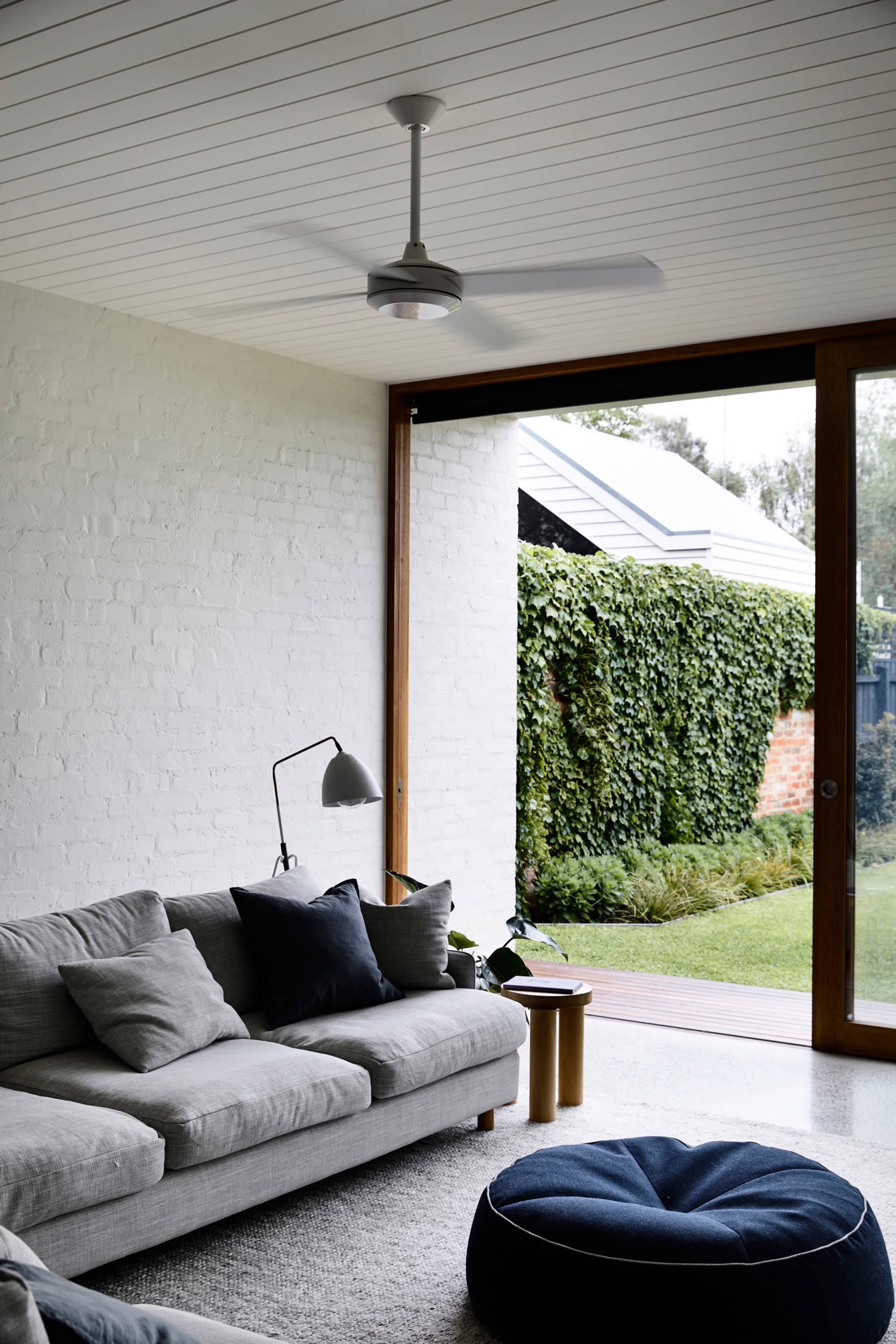 A modern living room features a gray sofa, a floor lamp, and a large window overlooking a green garden.