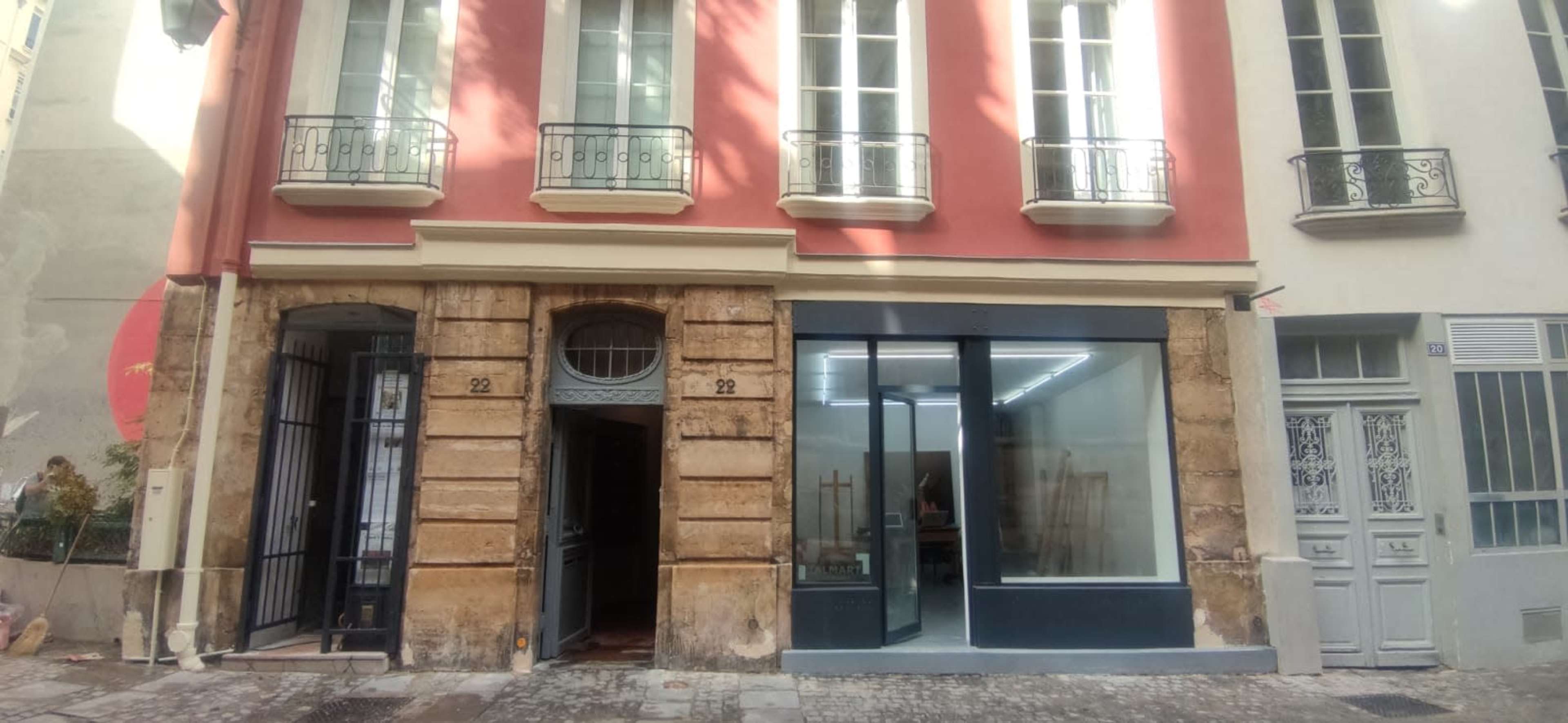 A two-story building with a brick facade and large windows, featuring a gallery-like entrance on the left and a modern storefront on the right.