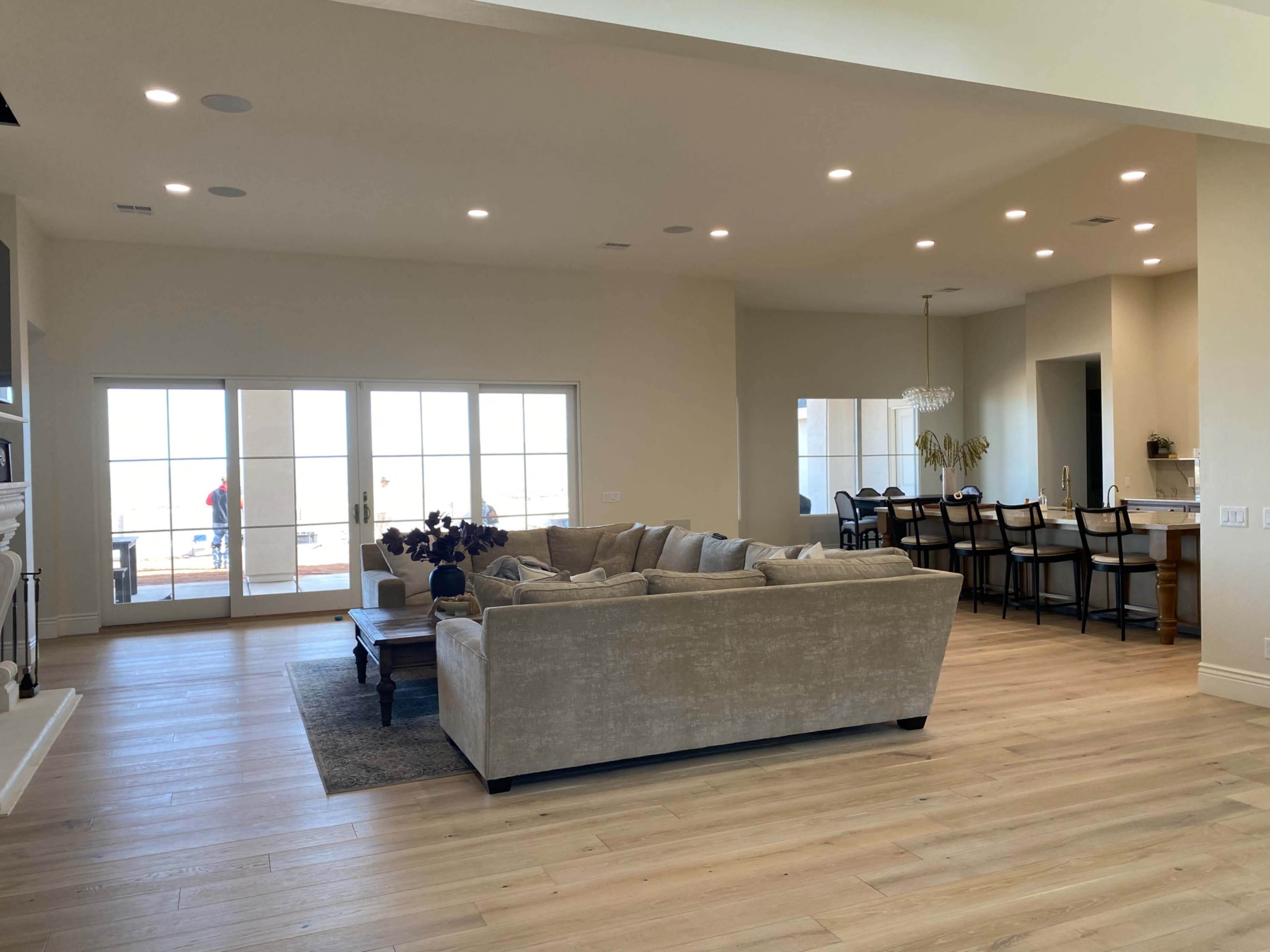 A spacious living room features a large sectional sofa and a dining area in an open floor plan with large windows.