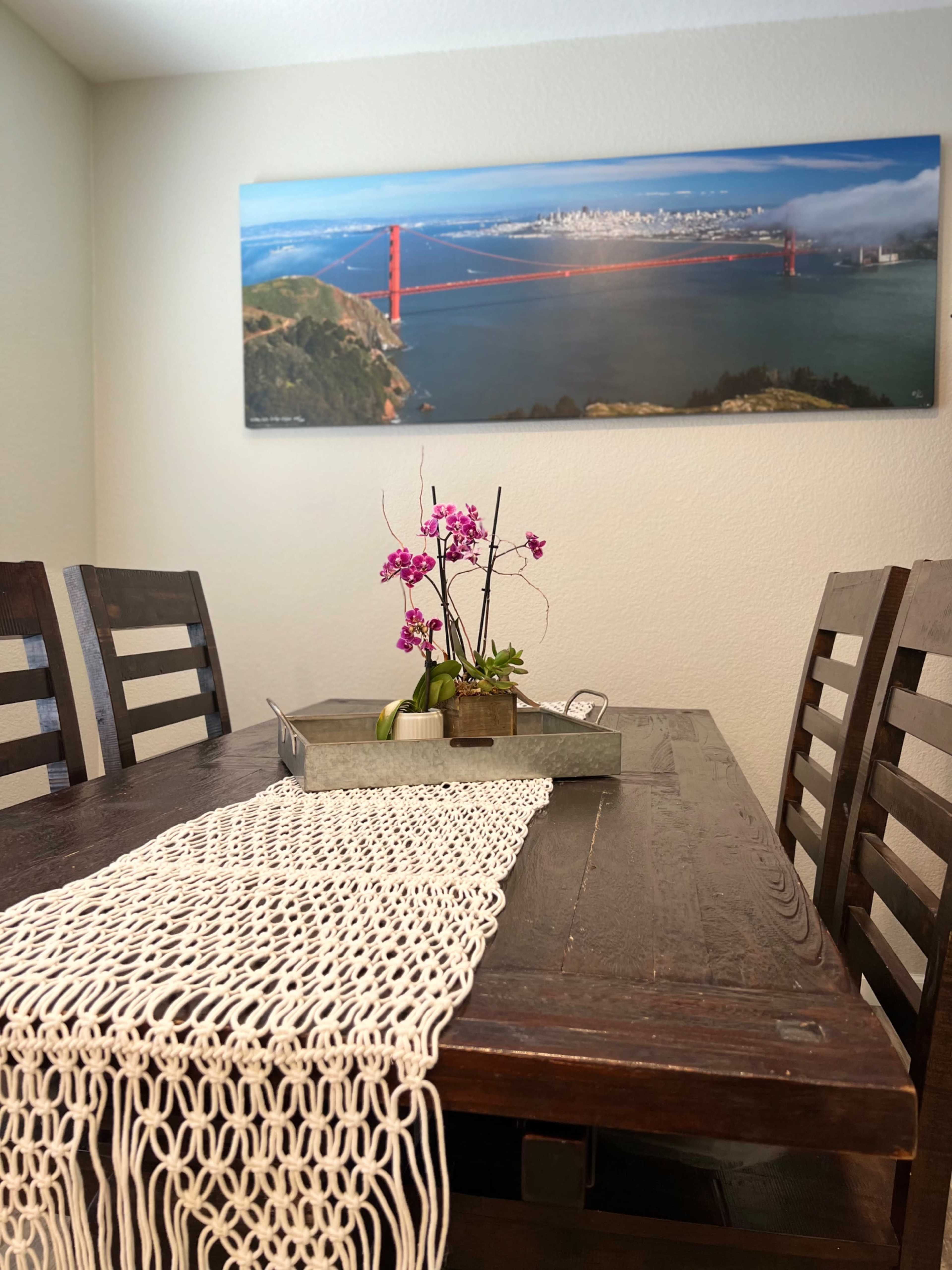 A dining table with a decorative centerpiece of flowers and a table runner, set against a wall featuring a panoramic photo of the Golden Gate Bridge.