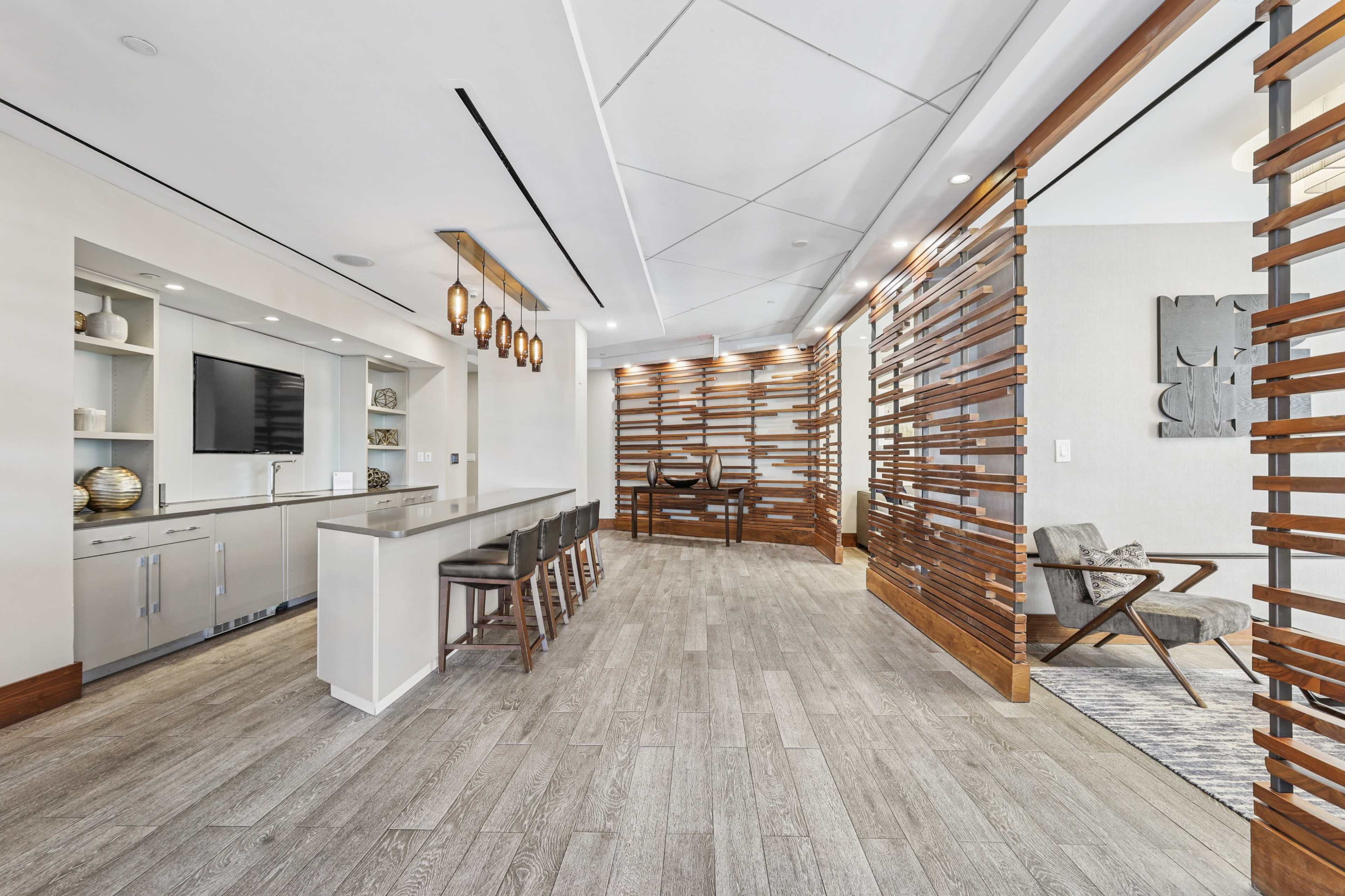 The image shows a modern interior space featuring a kitchen island with barstools, a living area with a chair, and decorative wooden dividers separating different sections.
