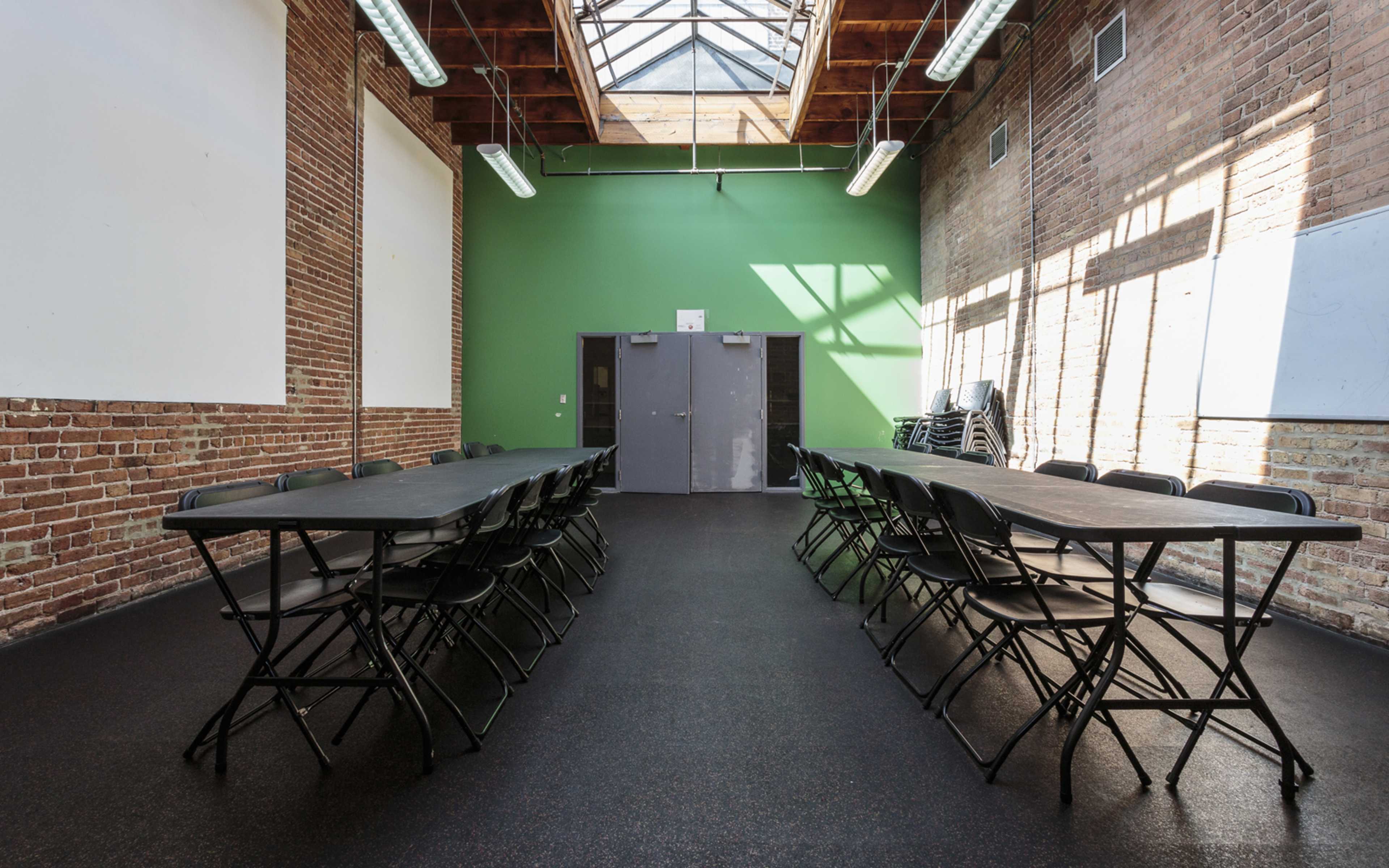 A spacious room with brick walls, two rows of folding tables, and a skylight overhead.