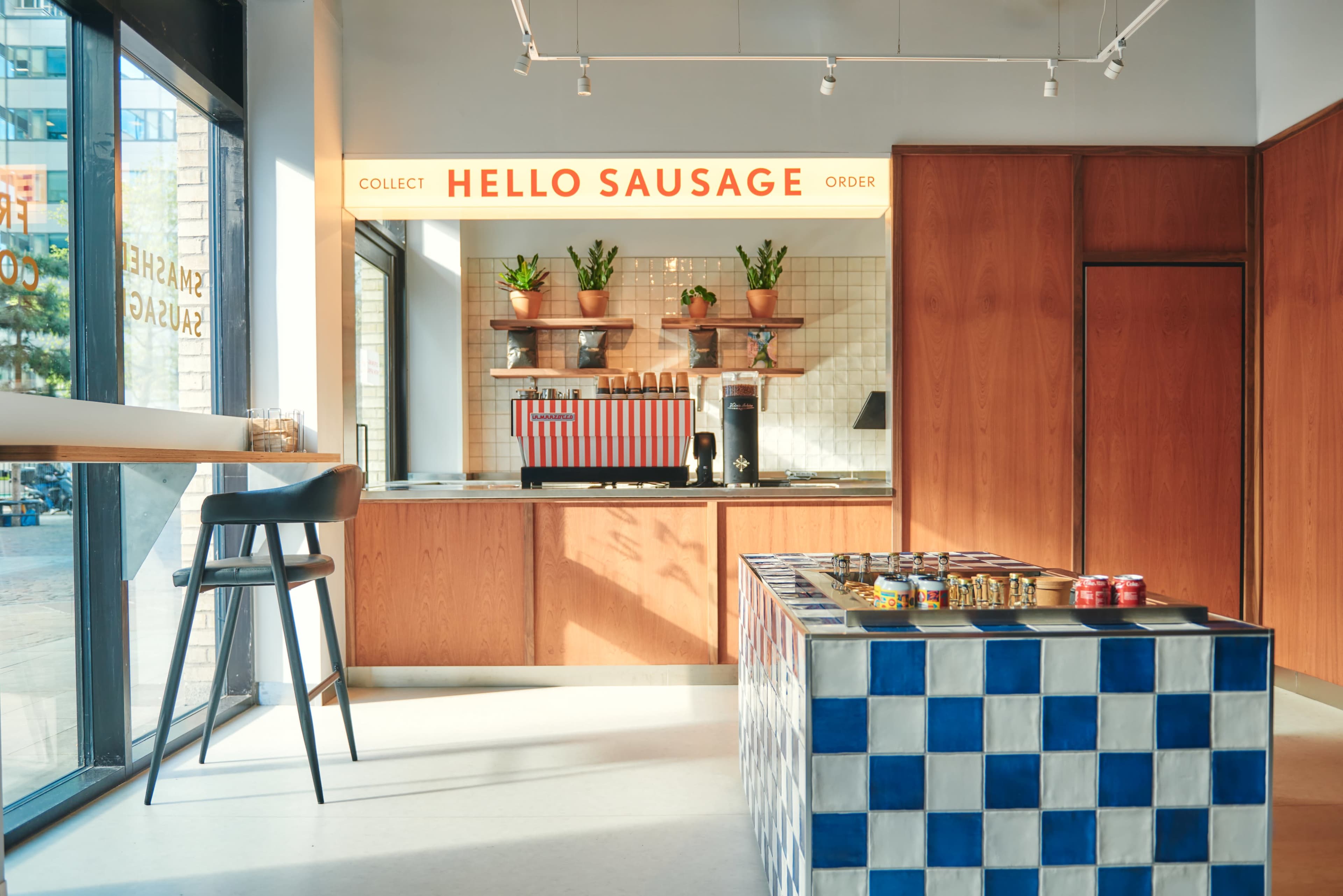 A modern food service area with a counter displaying products, potted plants on shelves, and a blue and white patterned table in the center.