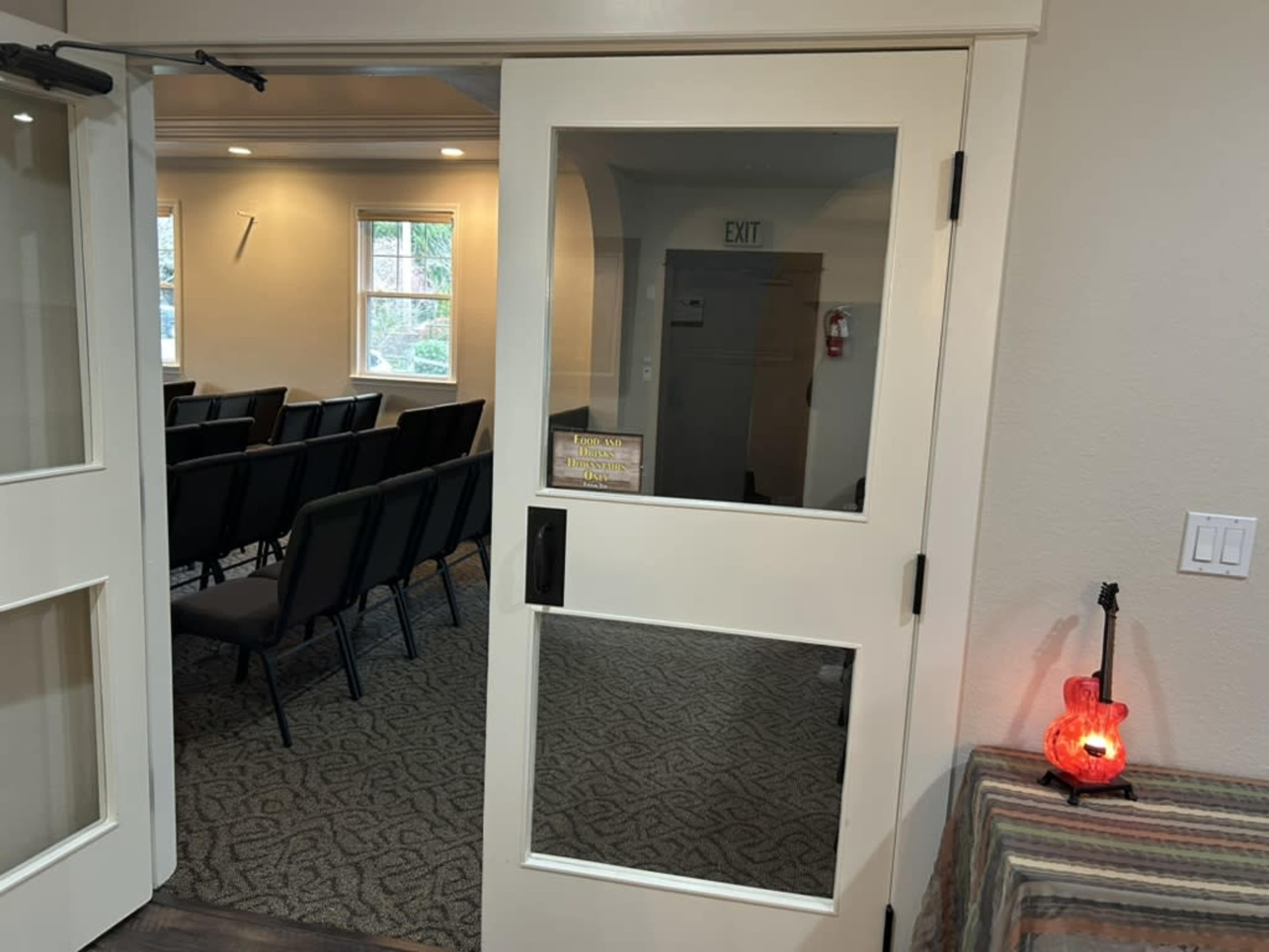 A doorway with glass panels leads into a room filled with rows of chairs, with an exit sign visible in the background.