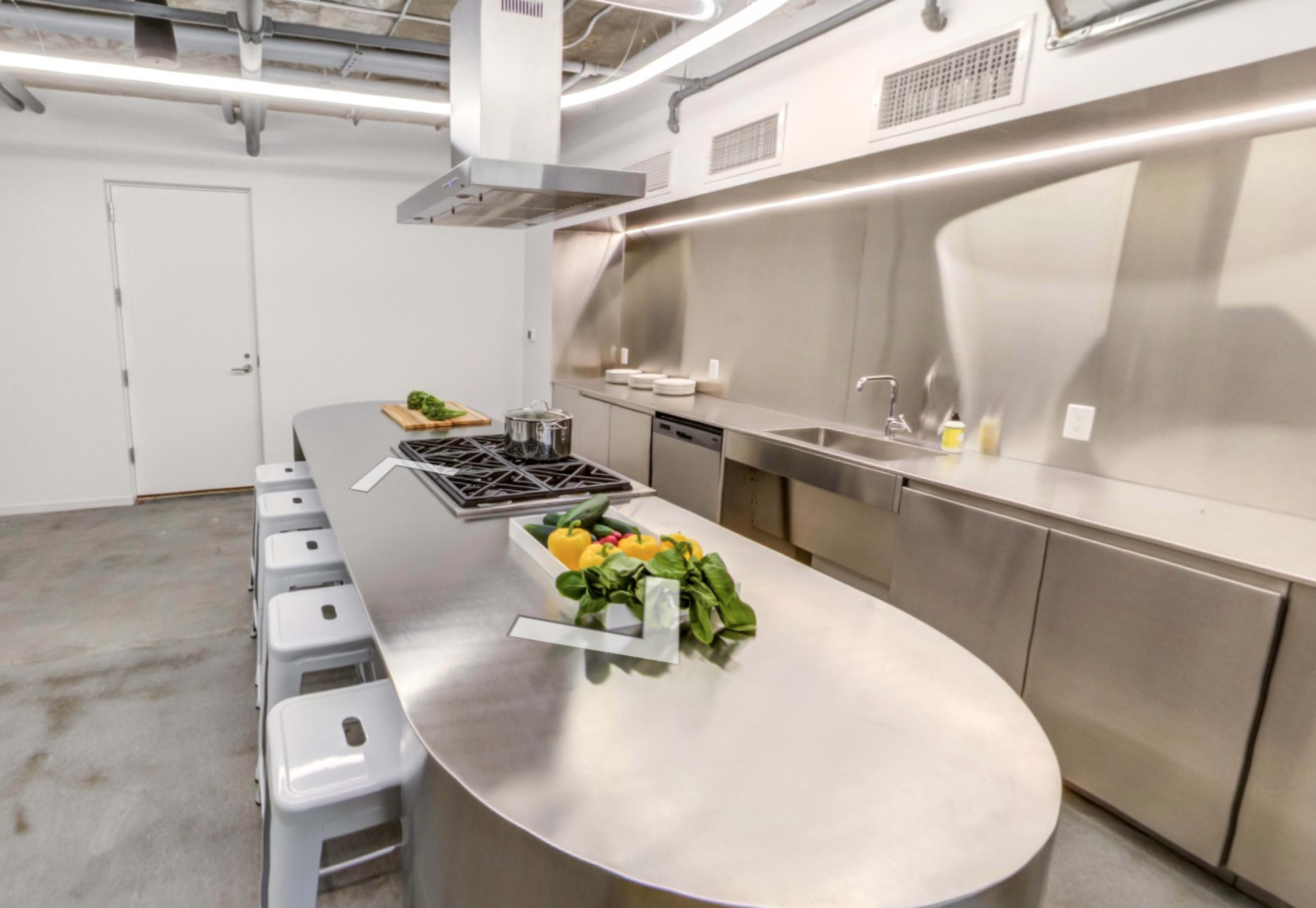A modern kitchen with a stainless steel island, several bar stools, and sleek appliances arranged along a wall.