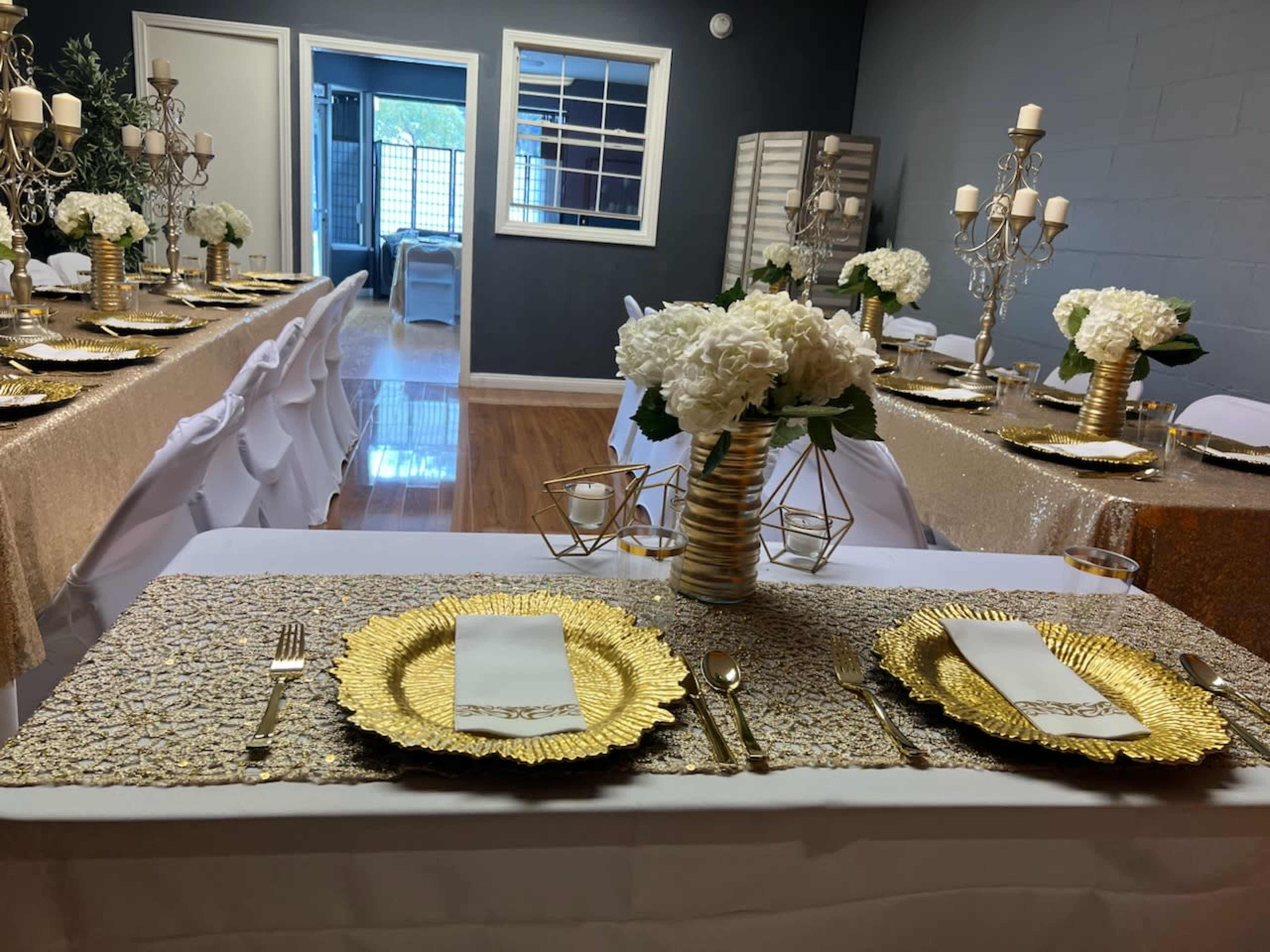 A decorated dining area features tables set with gold tableware, white floral centerpieces, and elegant candle holders.