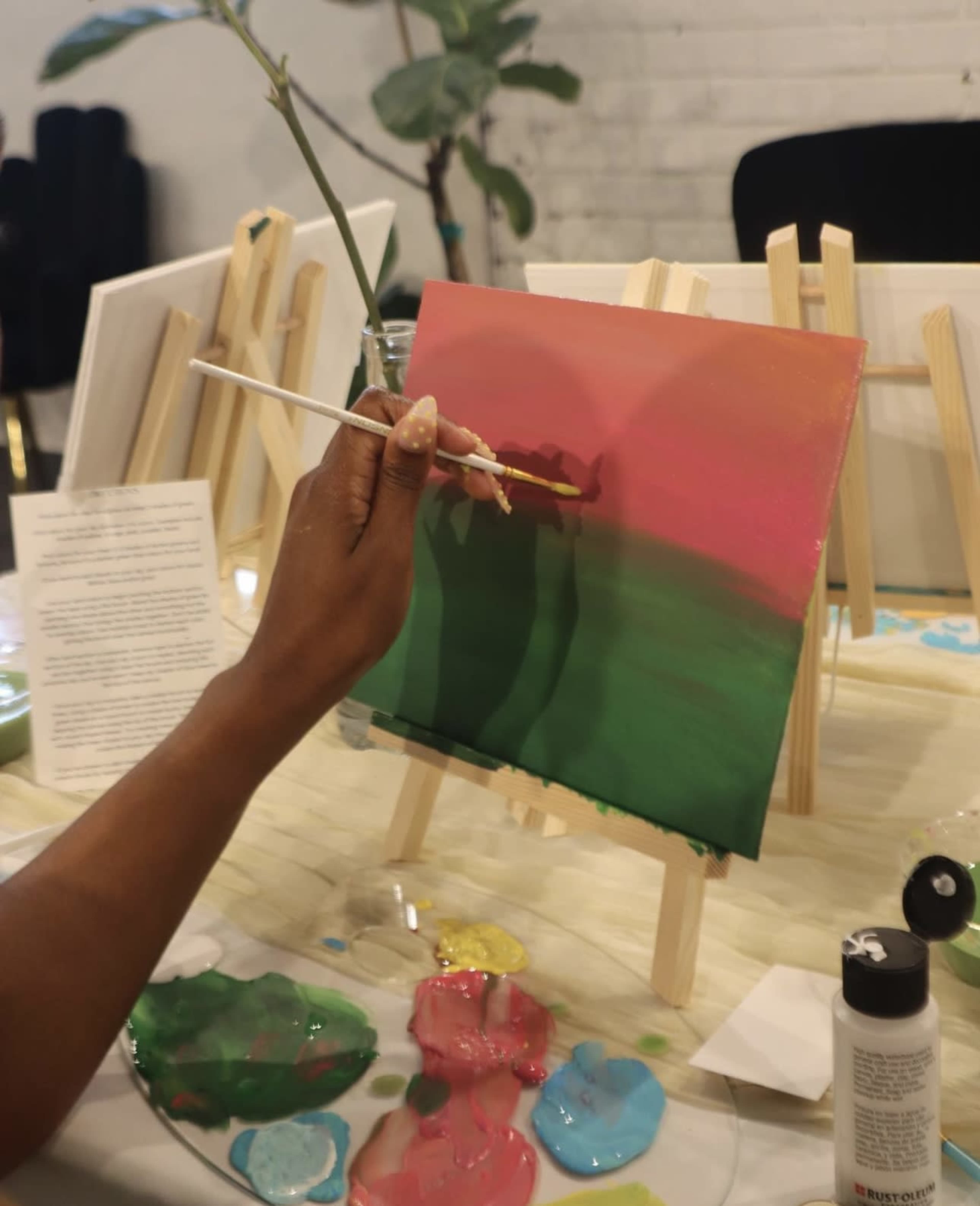 A person is painting on a canvas set on an easel, with various colors of paint spread out on a palette nearby.