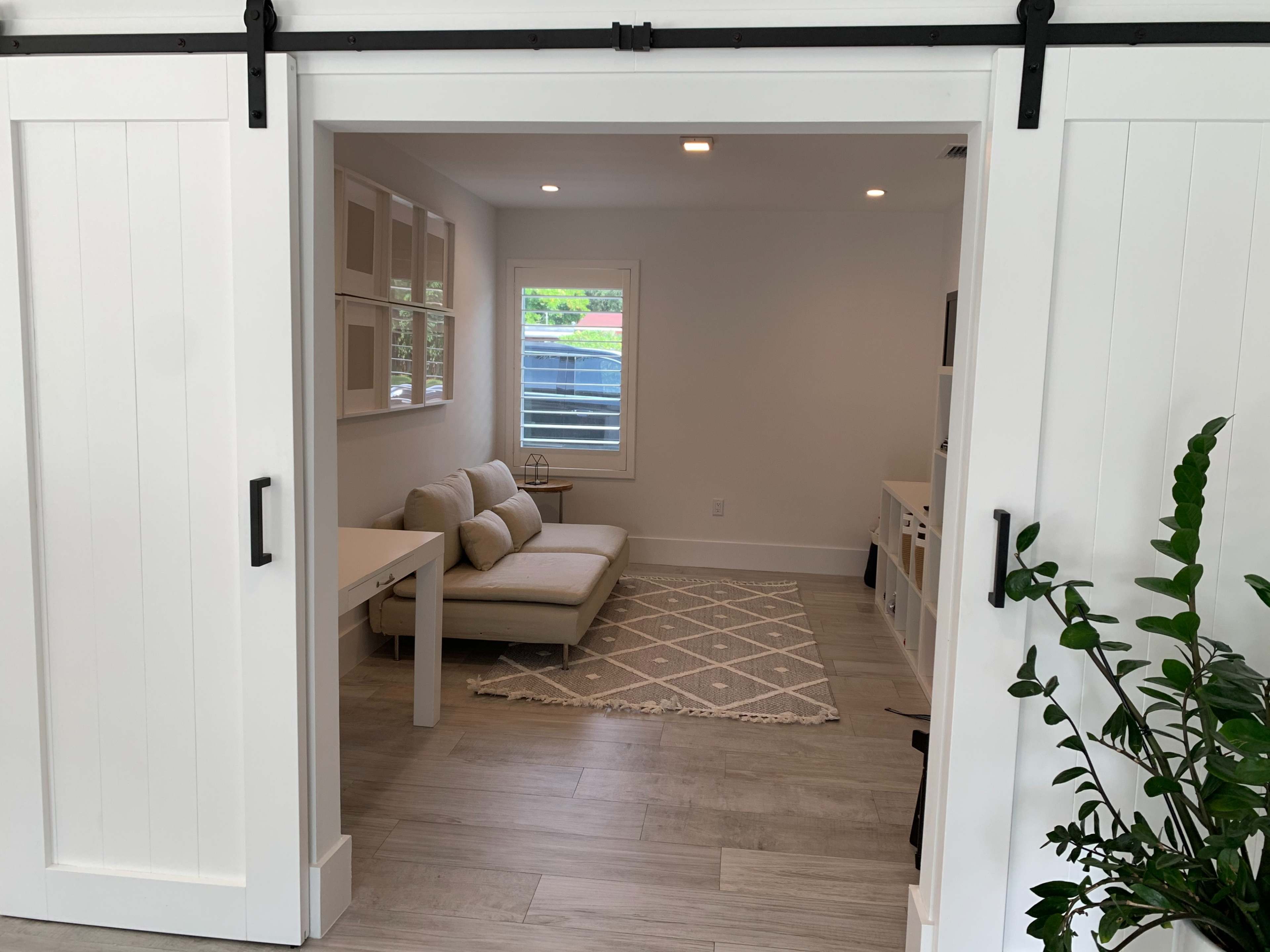 A light-colored room features a sofa, a small table, a patterned rug, and large sliding doors opening into the space.
