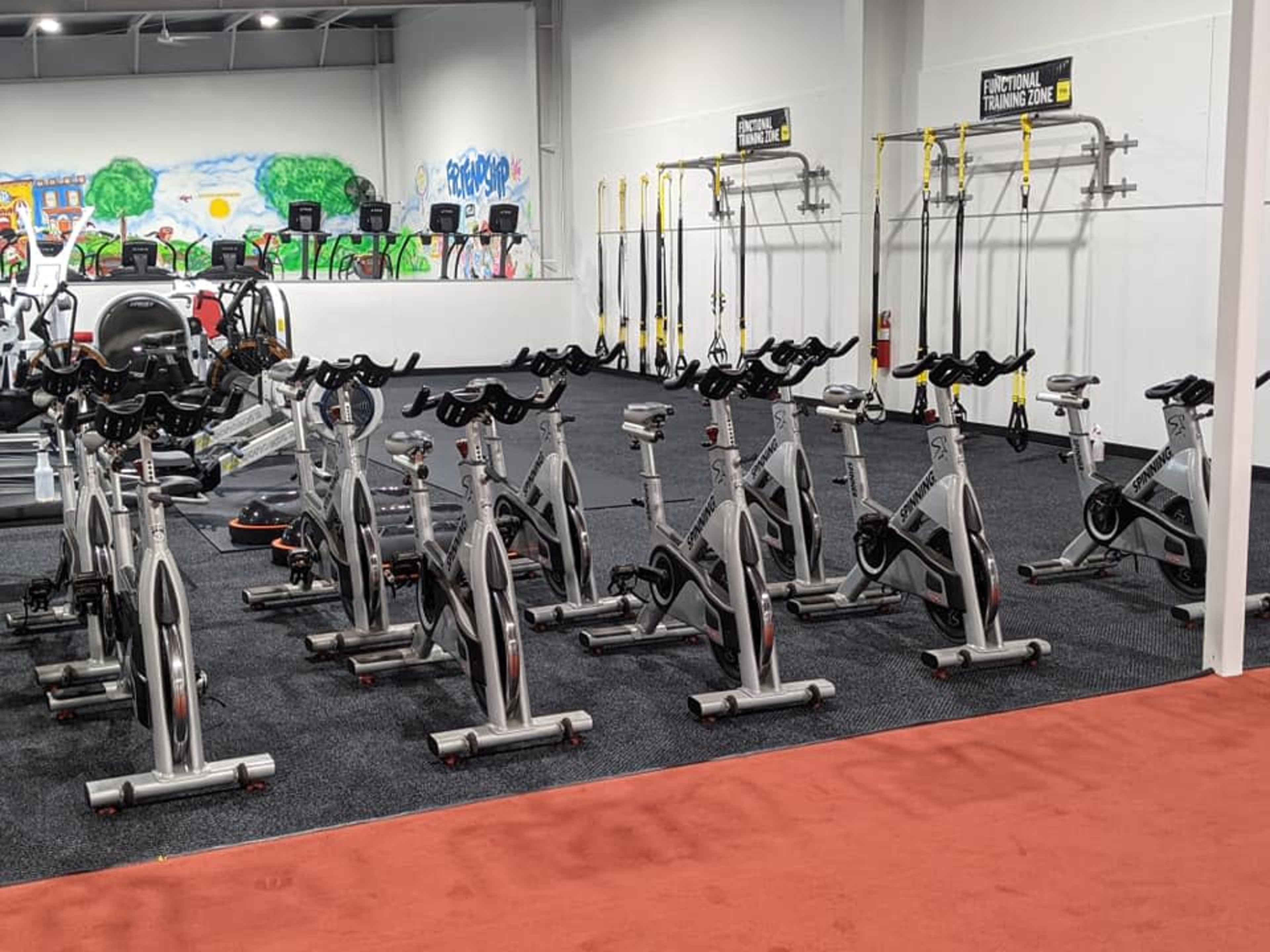 A gym area with several stationary bikes arranged in rows, alongside various fitness equipment against colorful wall murals.
