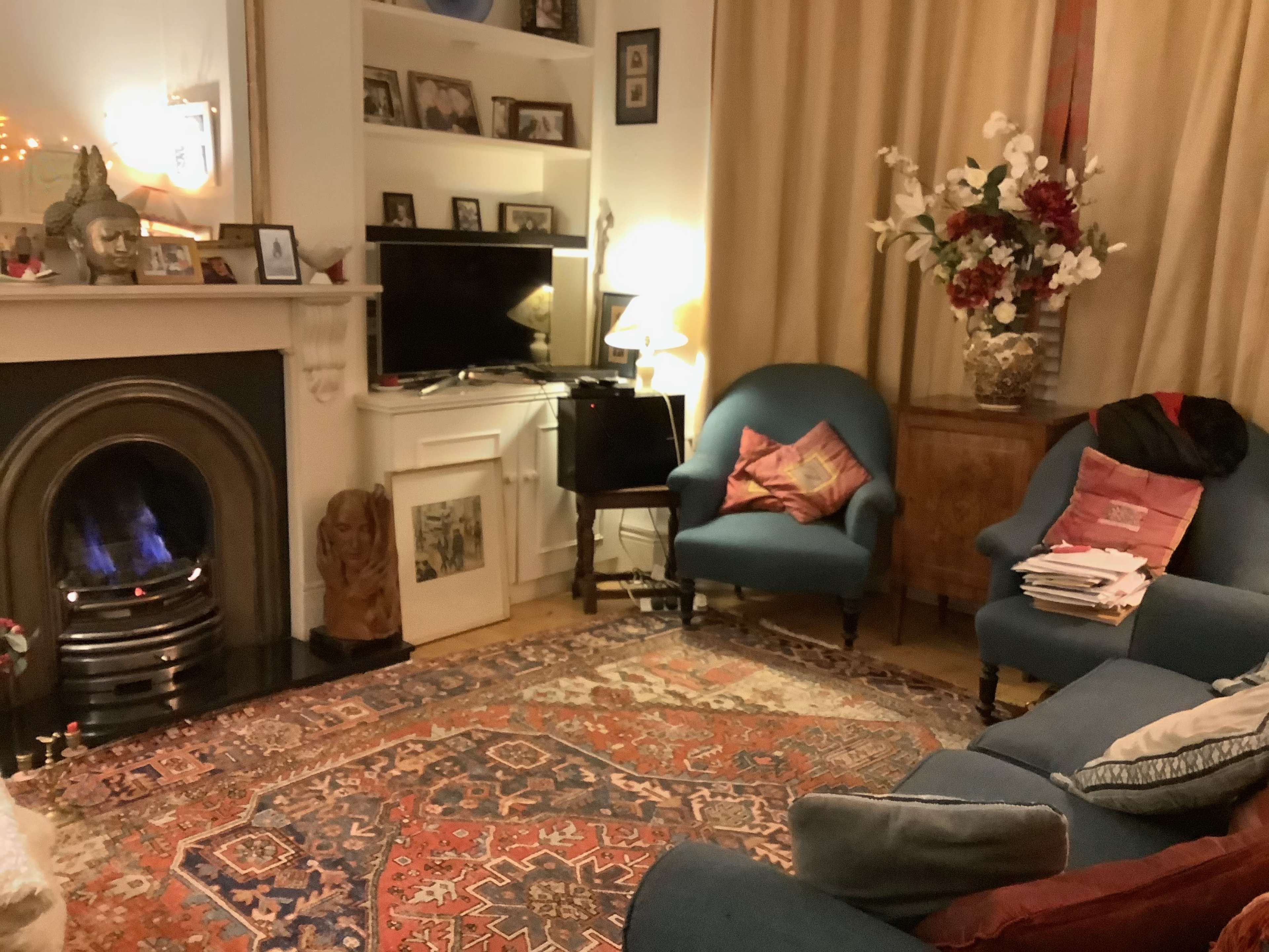 A cozy living room features a blue sofa and armchair, a decorative fireplace with a lion statue, a television, and a floral arrangement on a side table.