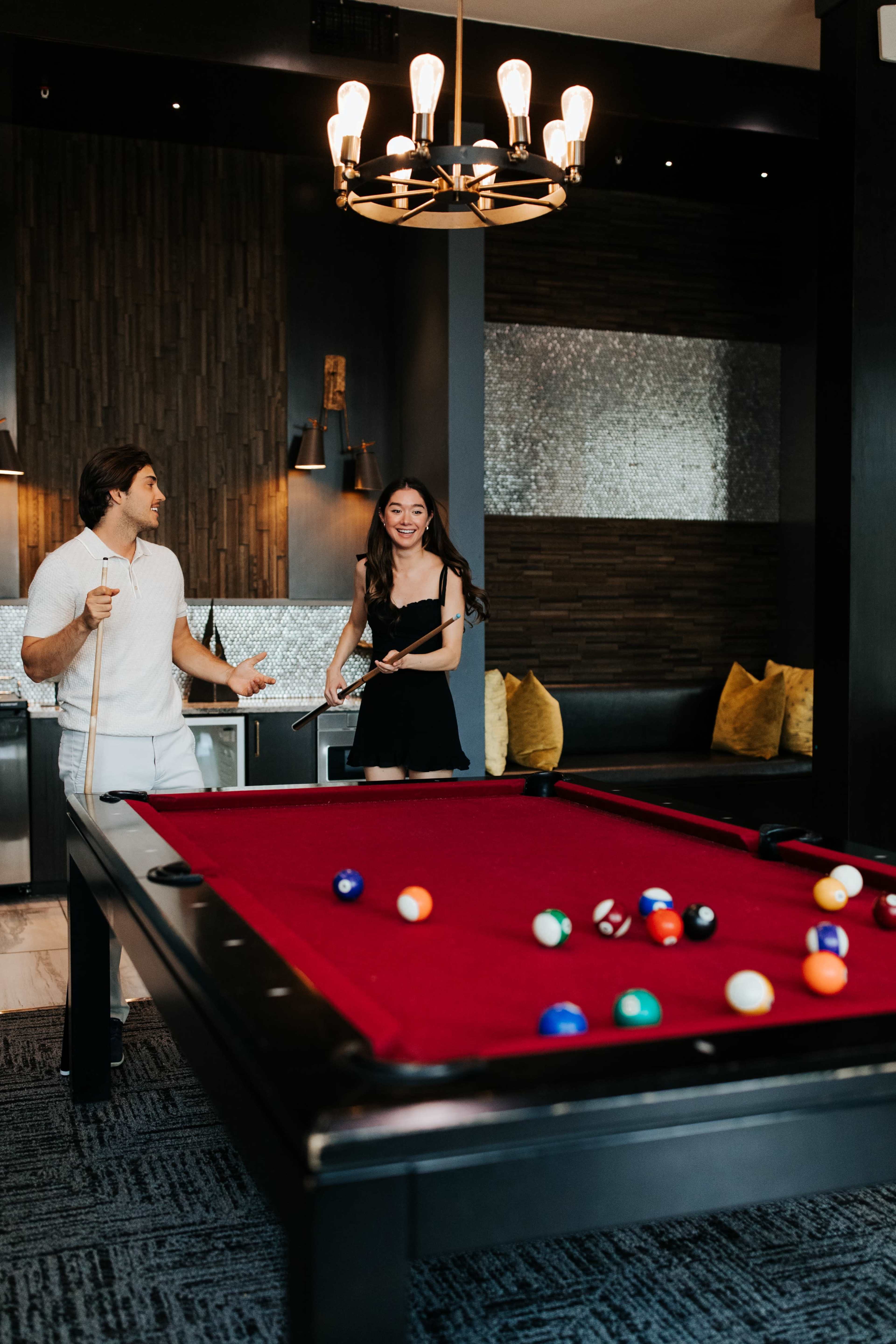 Two people are standing near a pool table with colorful balls scattered across the table in a modern game room.
