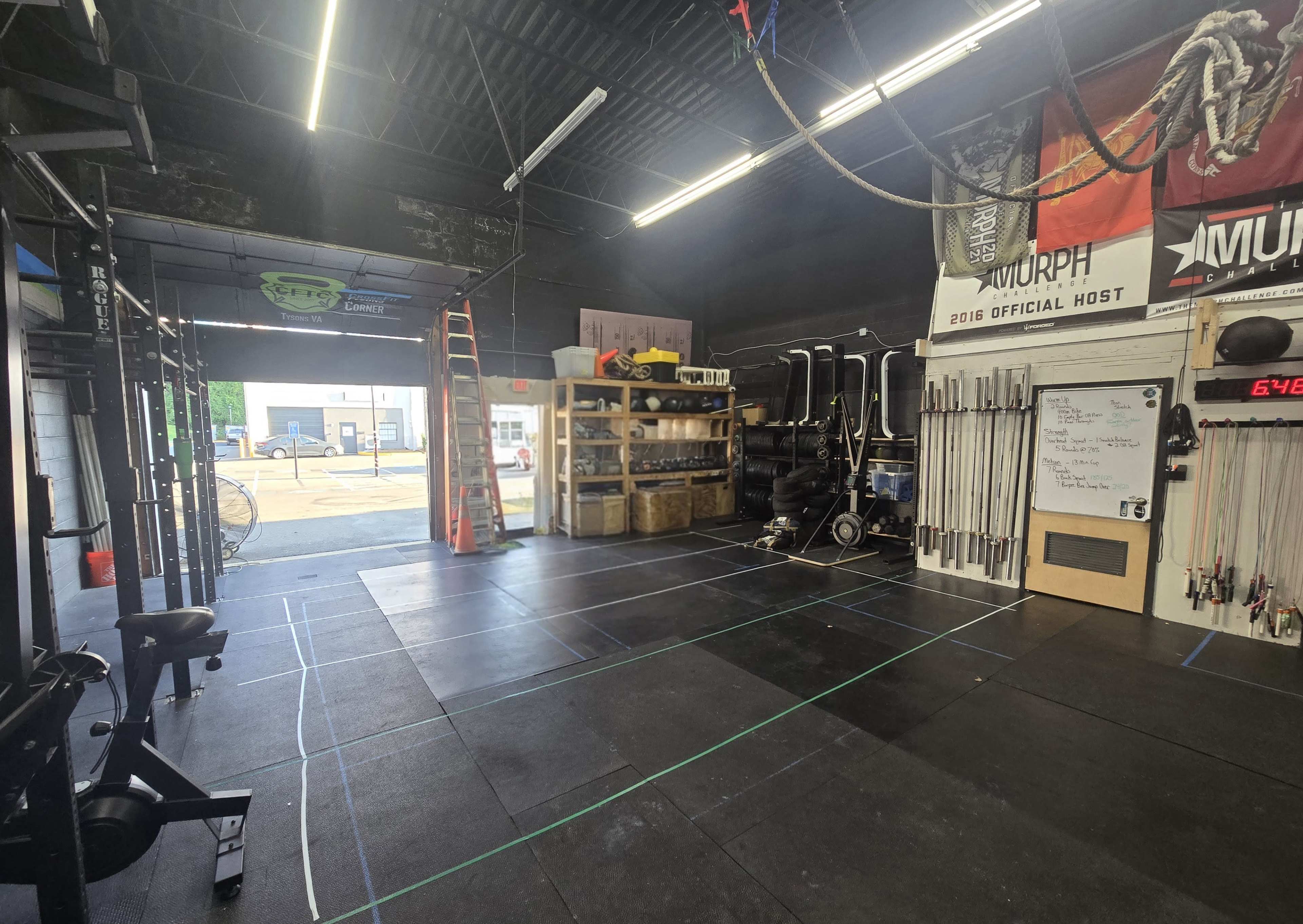 The image shows an indoor gym space with exercise equipment, a storage area against the wall, and a door leading outside.