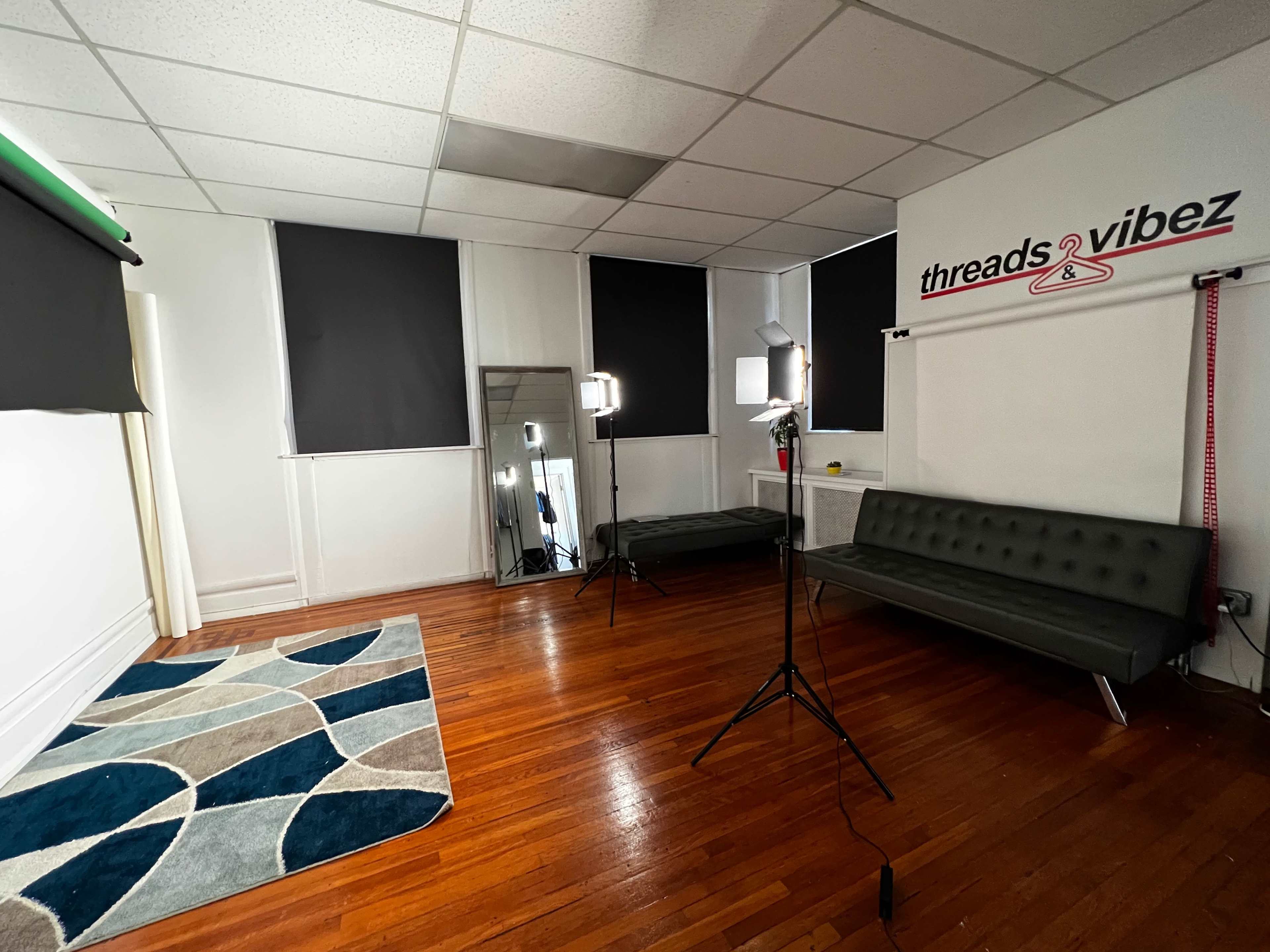 A well-lit studio space featuring a black sofa, a large mirror, and two light stands, with dark curtains covering the windows.