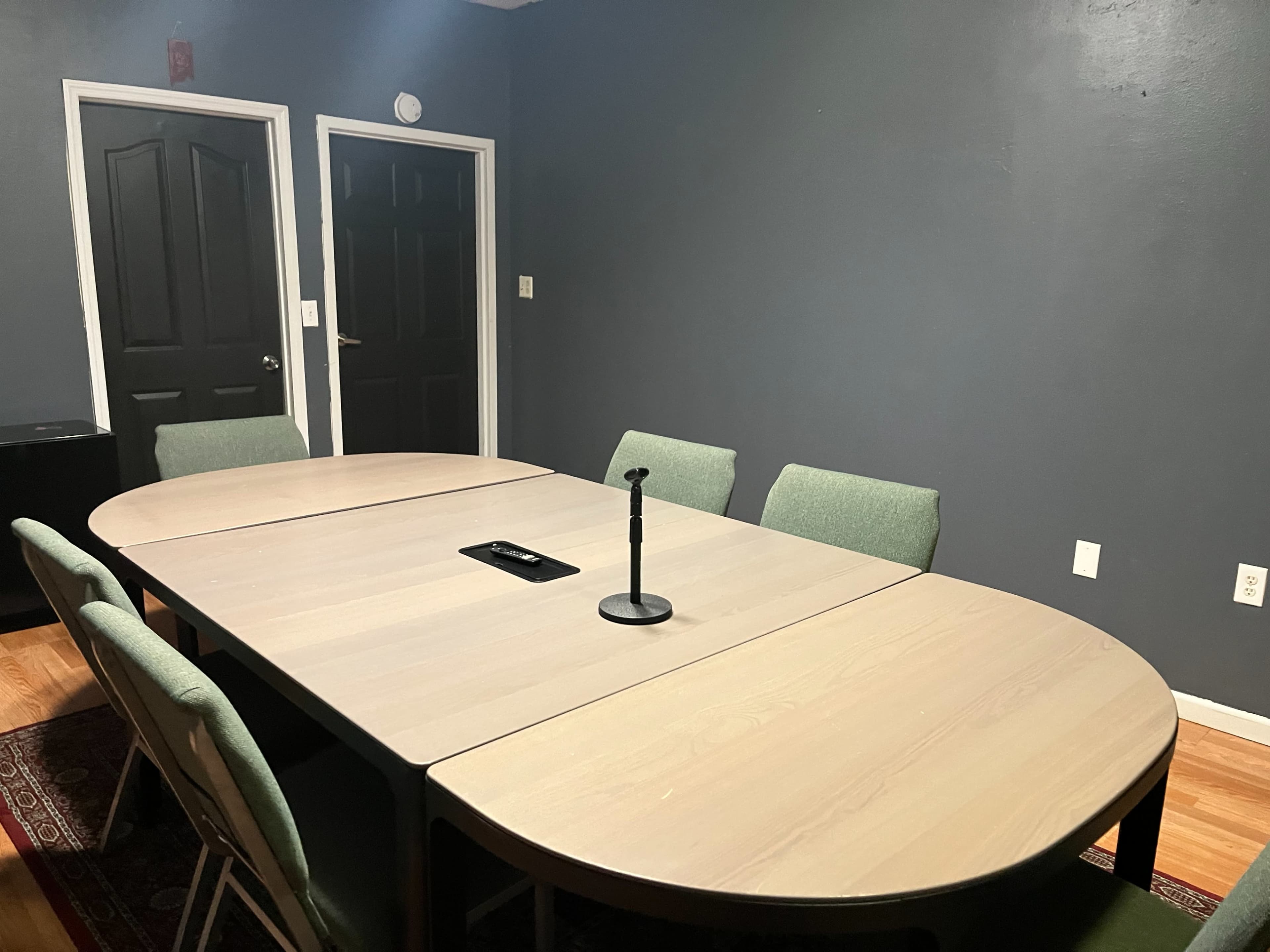 A rectangular conference table with a microphone in the center is surrounded by several chairs in a dimly lit meeting room.