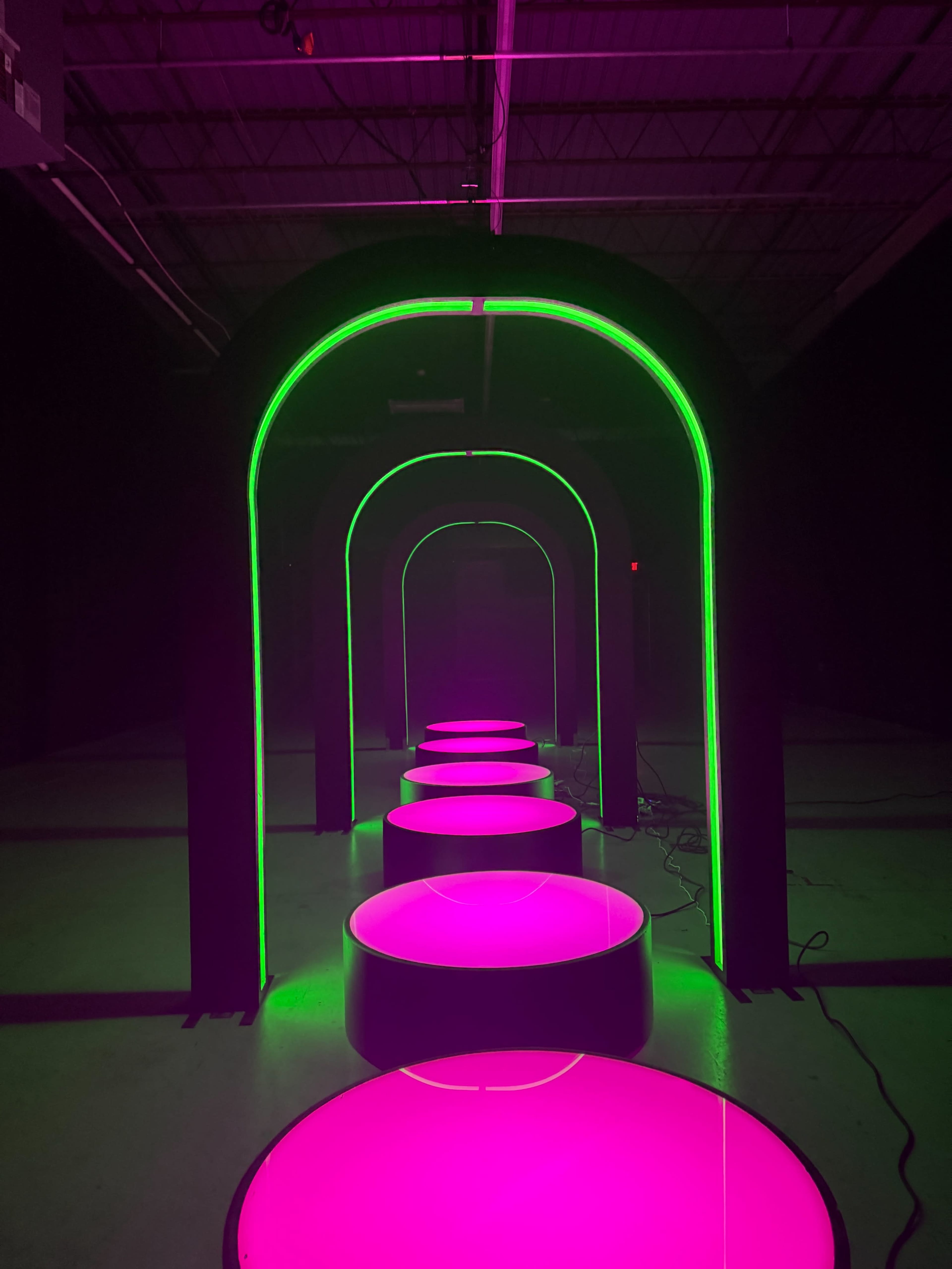 The image shows a series of illuminated arches with bright pink circular platforms arranged in a linear formation.