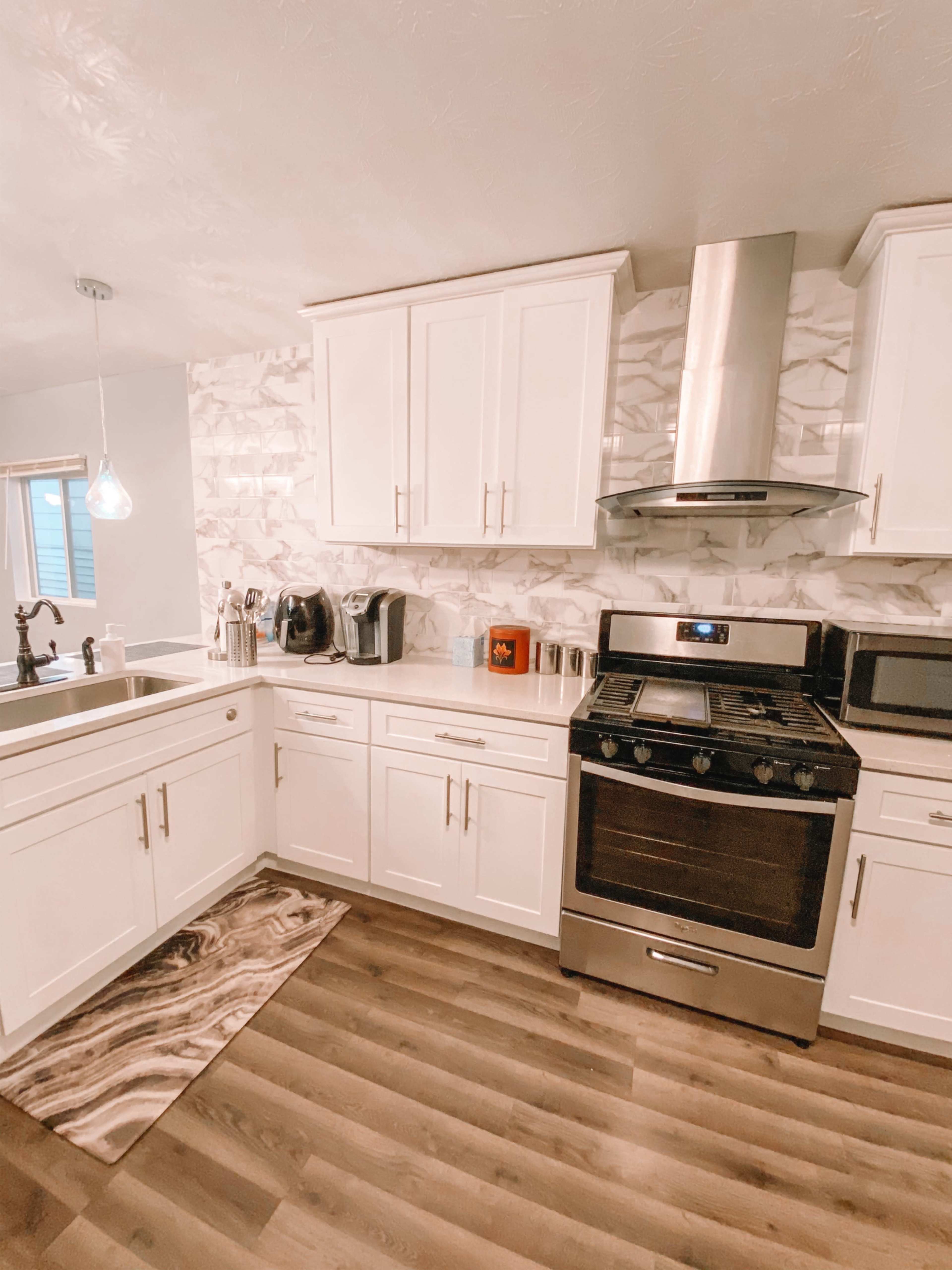 A modern kitchen with white cabinets, a stainless steel stove, and a patterned rug on the wooden floor.