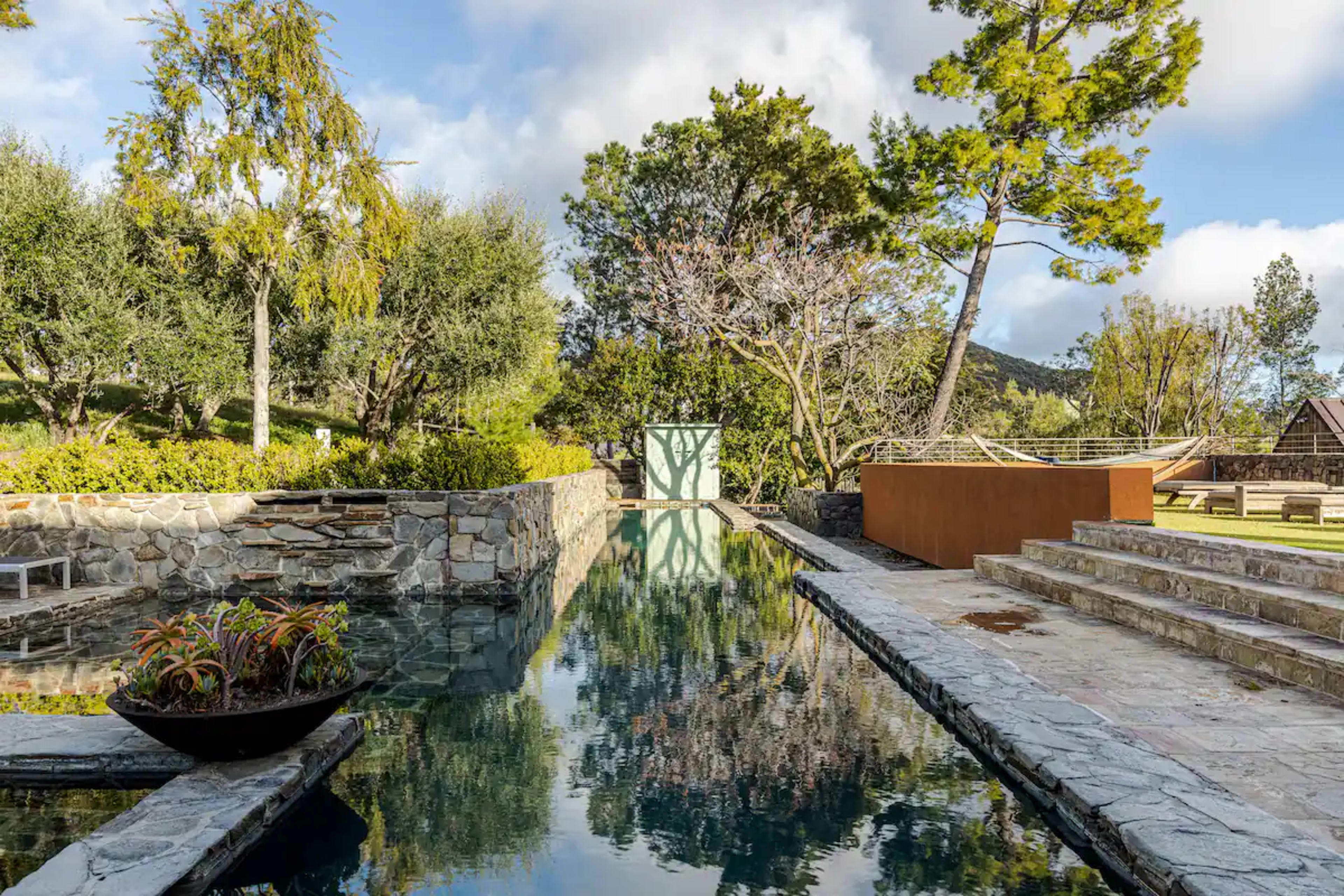 The image features a serene backyard with a stone pathway, reflecting pool, and landscaped greenery.