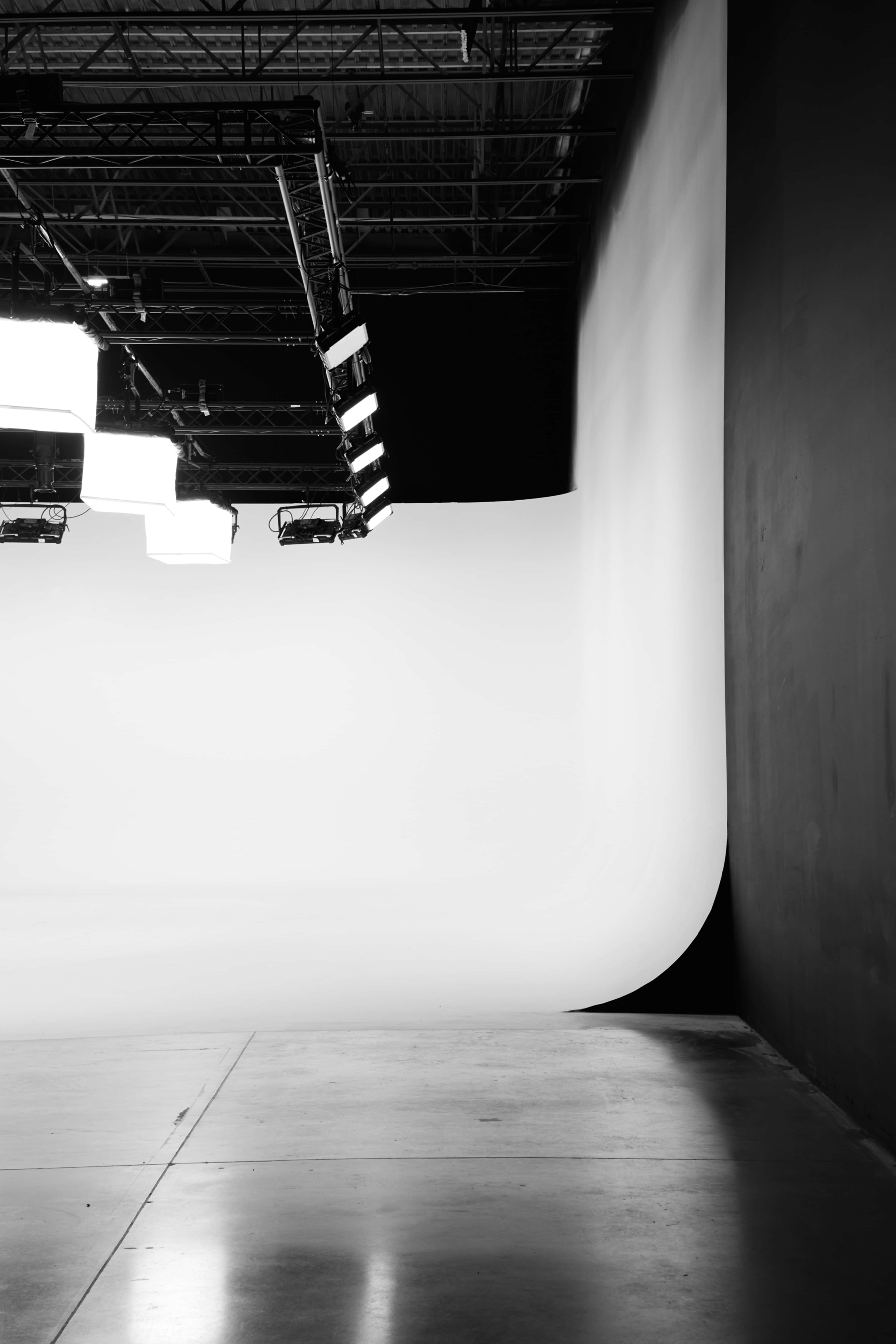 A spacious photo studio with a seamless white backdrop, soft lighting, and a smooth concrete floor.