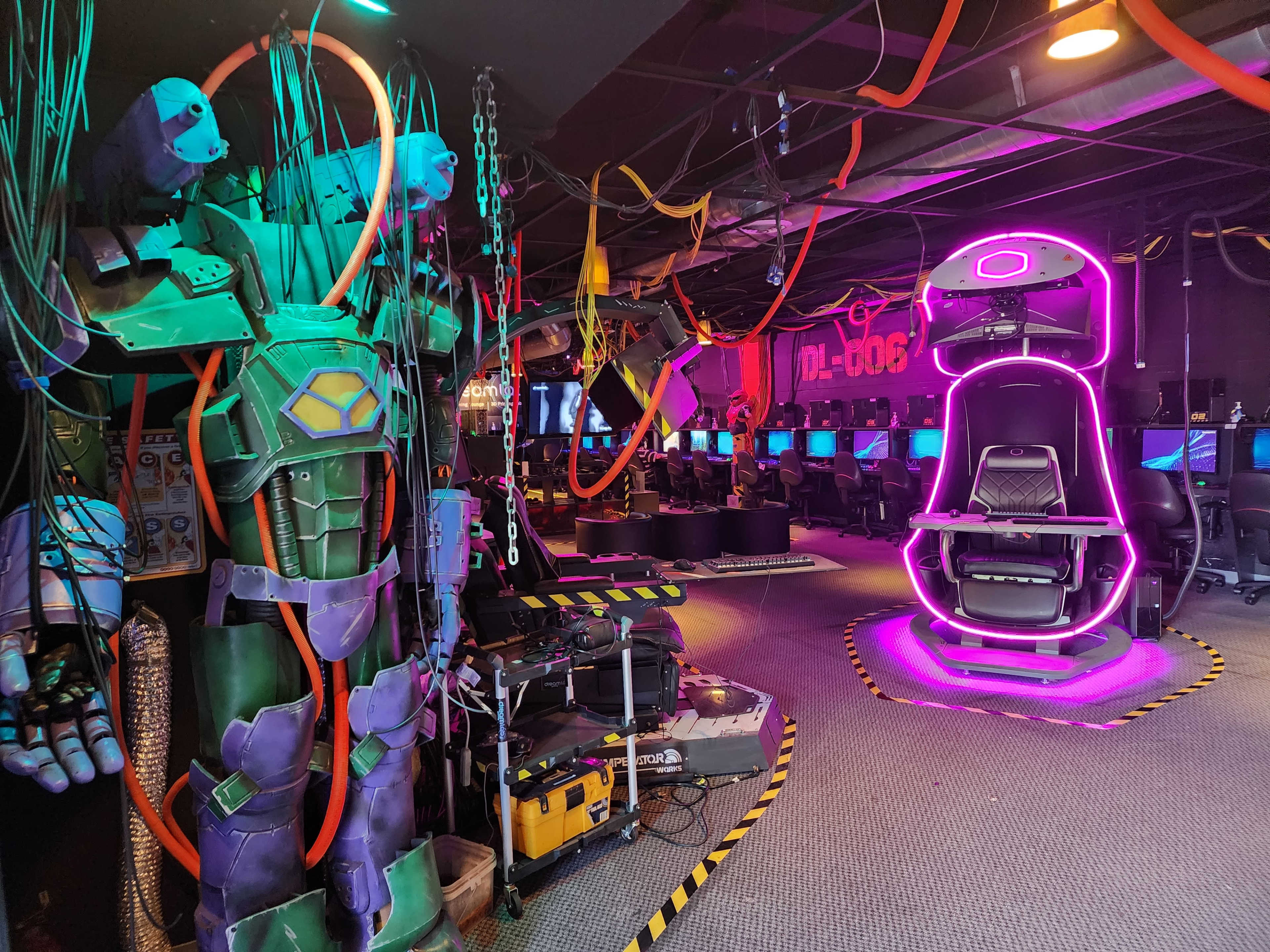 The image shows a gaming facility featuring futuristic machinery and gaming stations illuminated by vibrant neon lights.