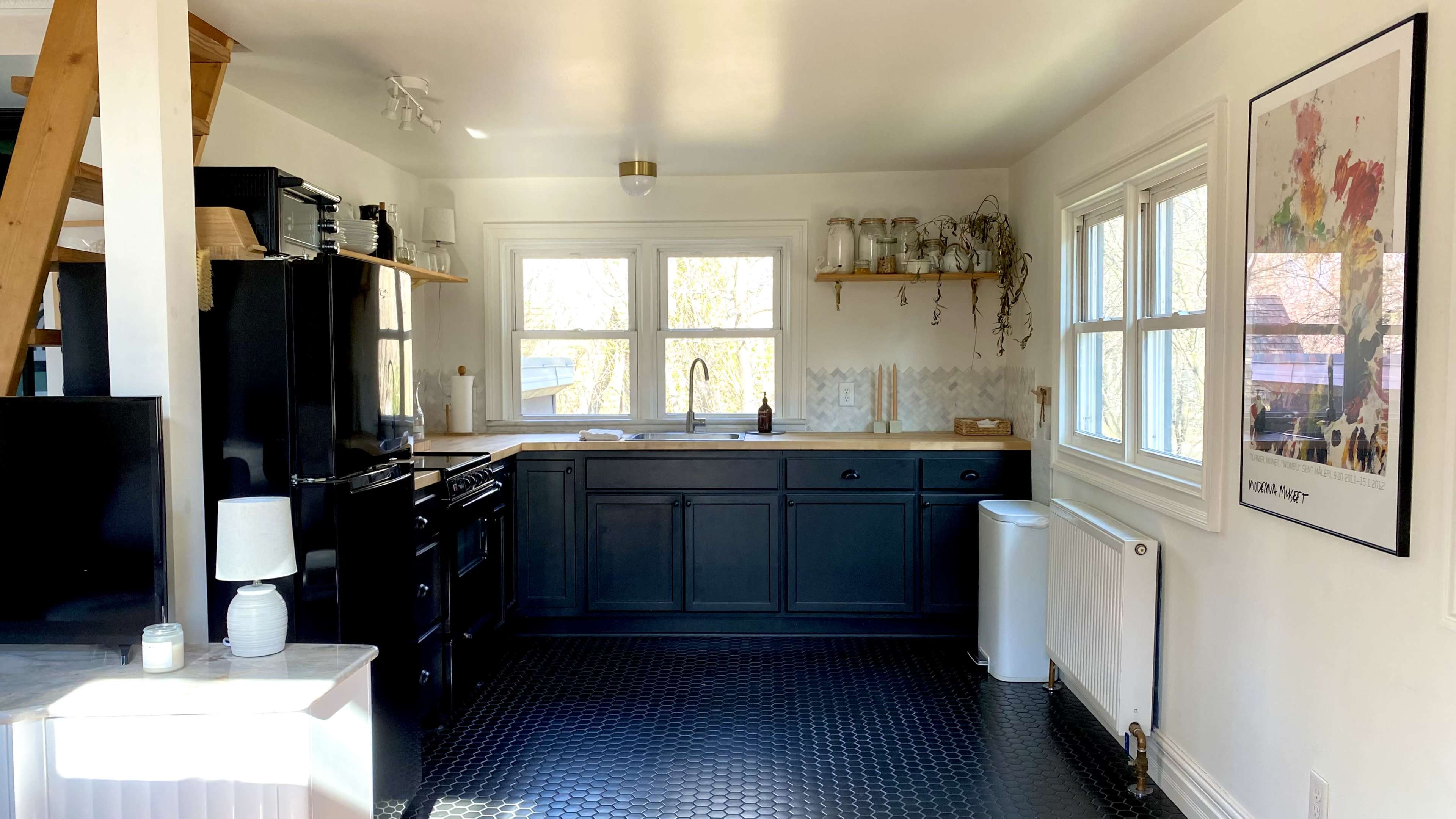 A modern kitchen features black cabinets, a black refrigerator, and a stove, with a wooden countertop and white walls.