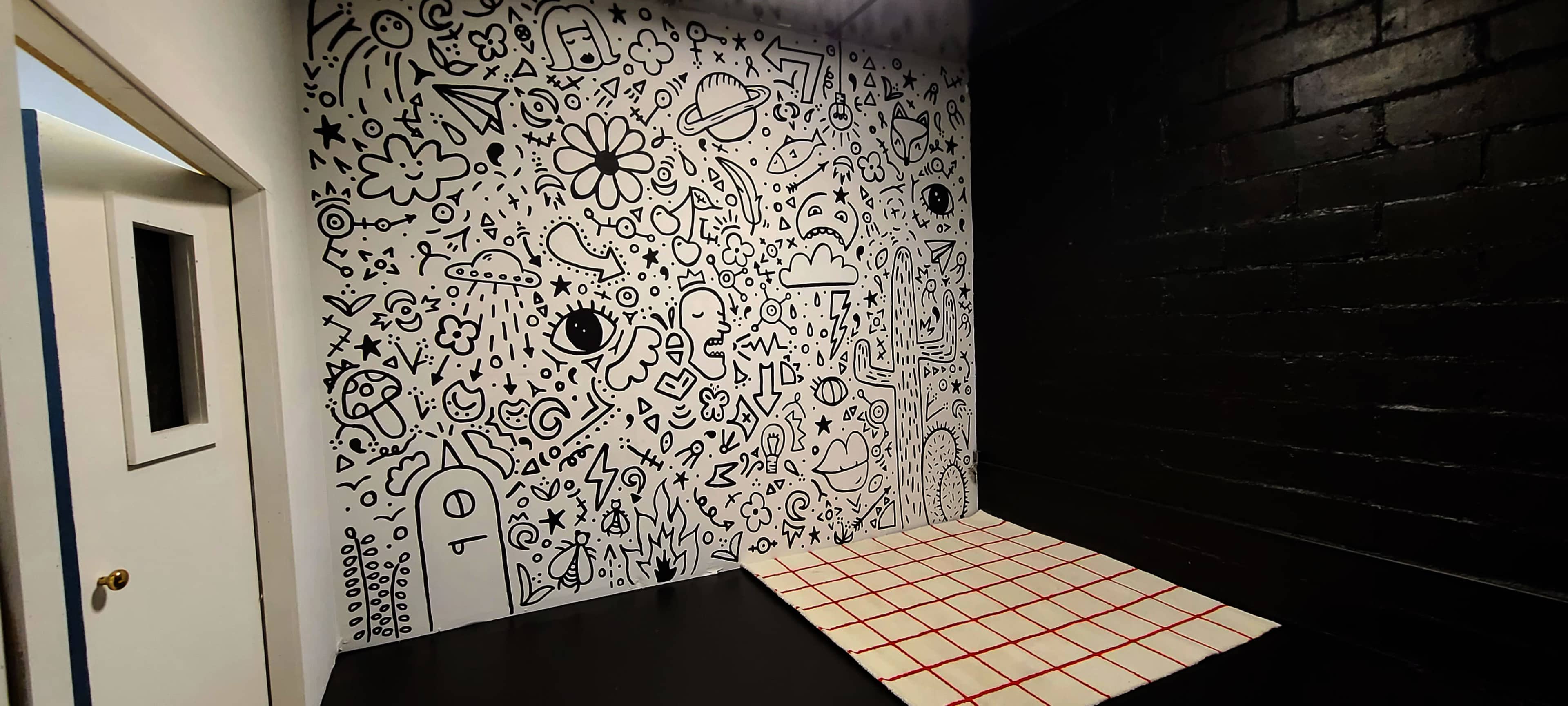 A corner of a room featuring a black wall with a white doodle mural and a floor with a red-grid design.