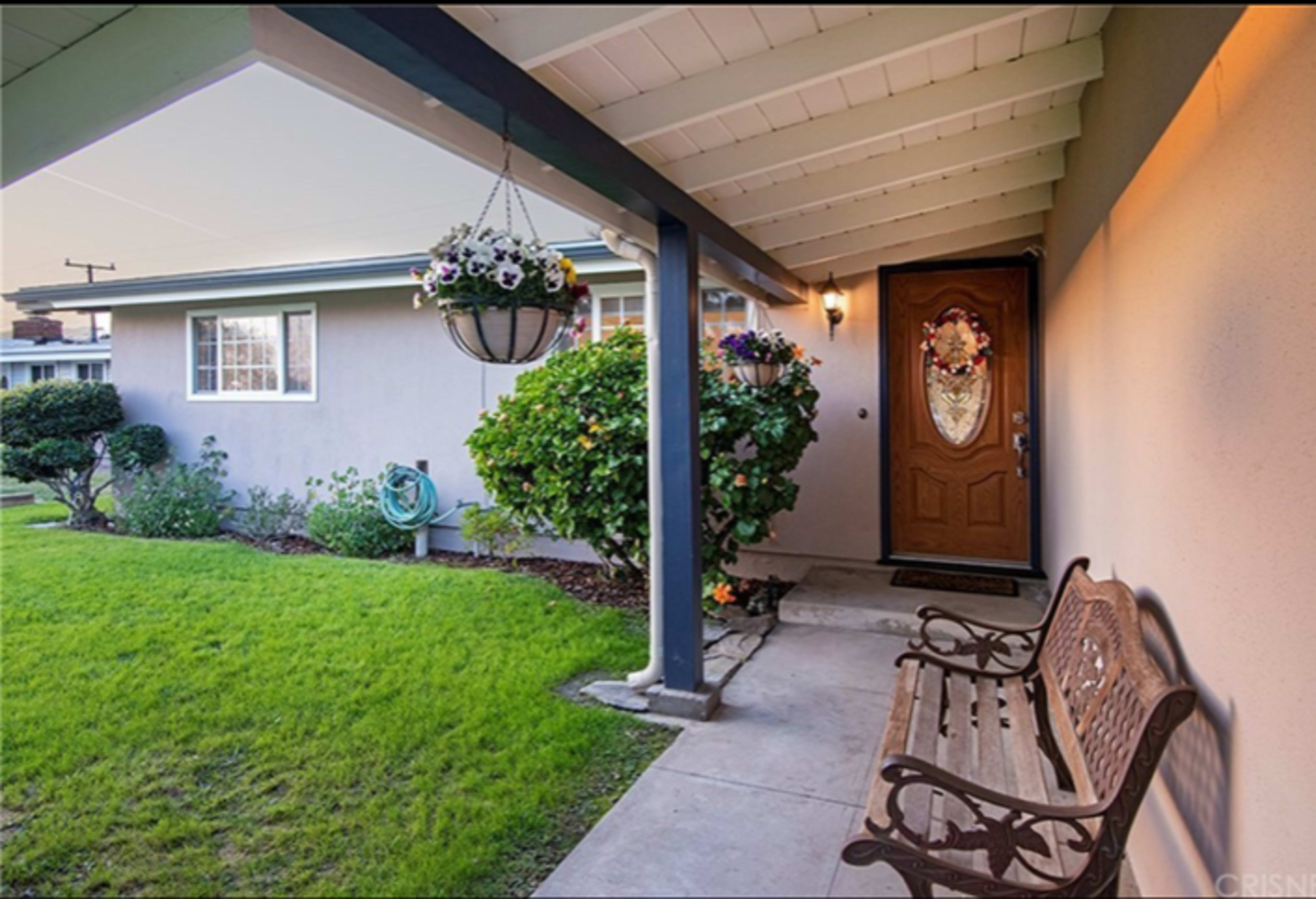 A front porch with a wooden bench, a decorative door, and potted plants beside a well-maintained lawn.