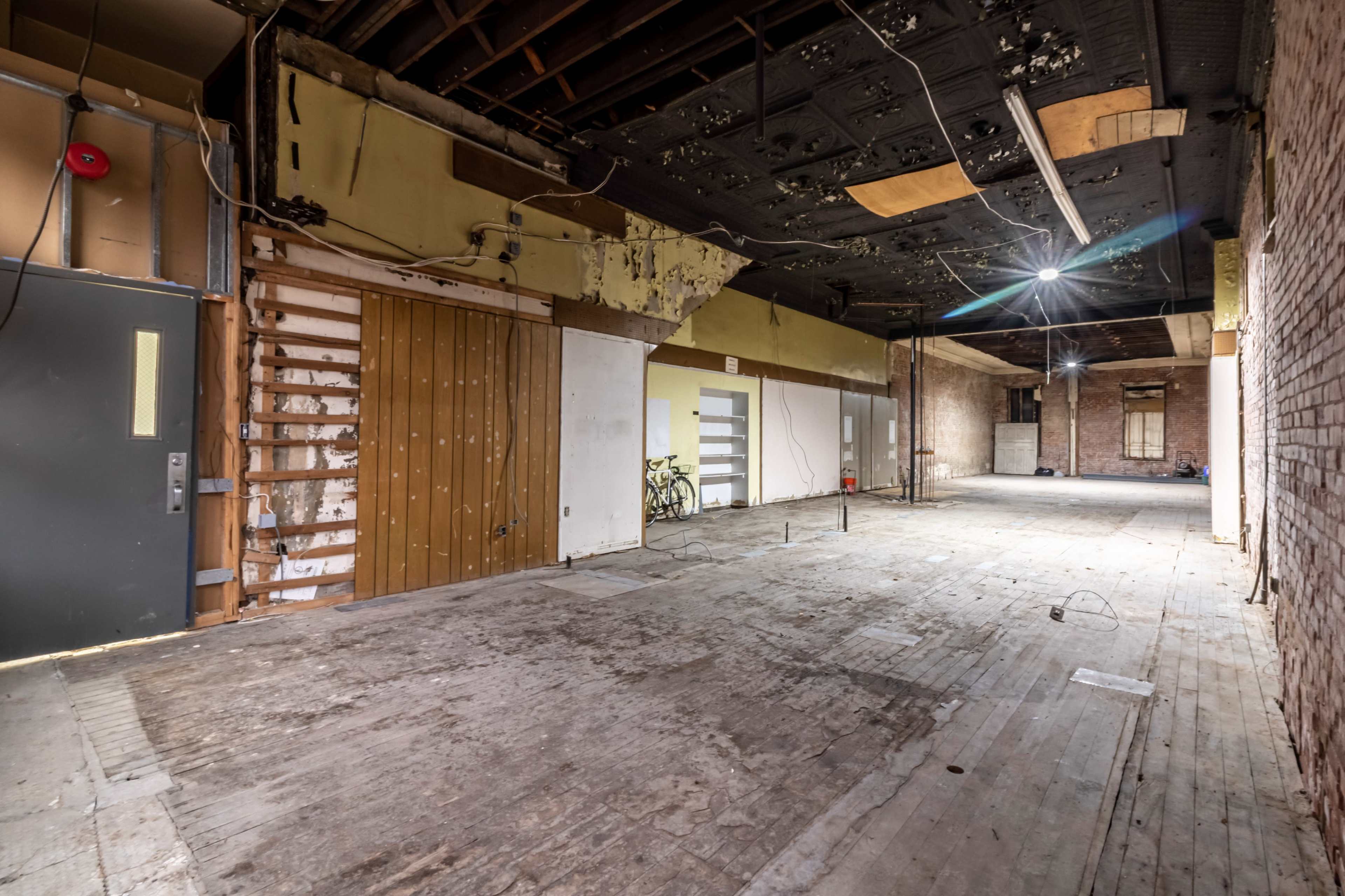 An empty interior space with exposed walls, a wooden floor, and unfinished ceilings.