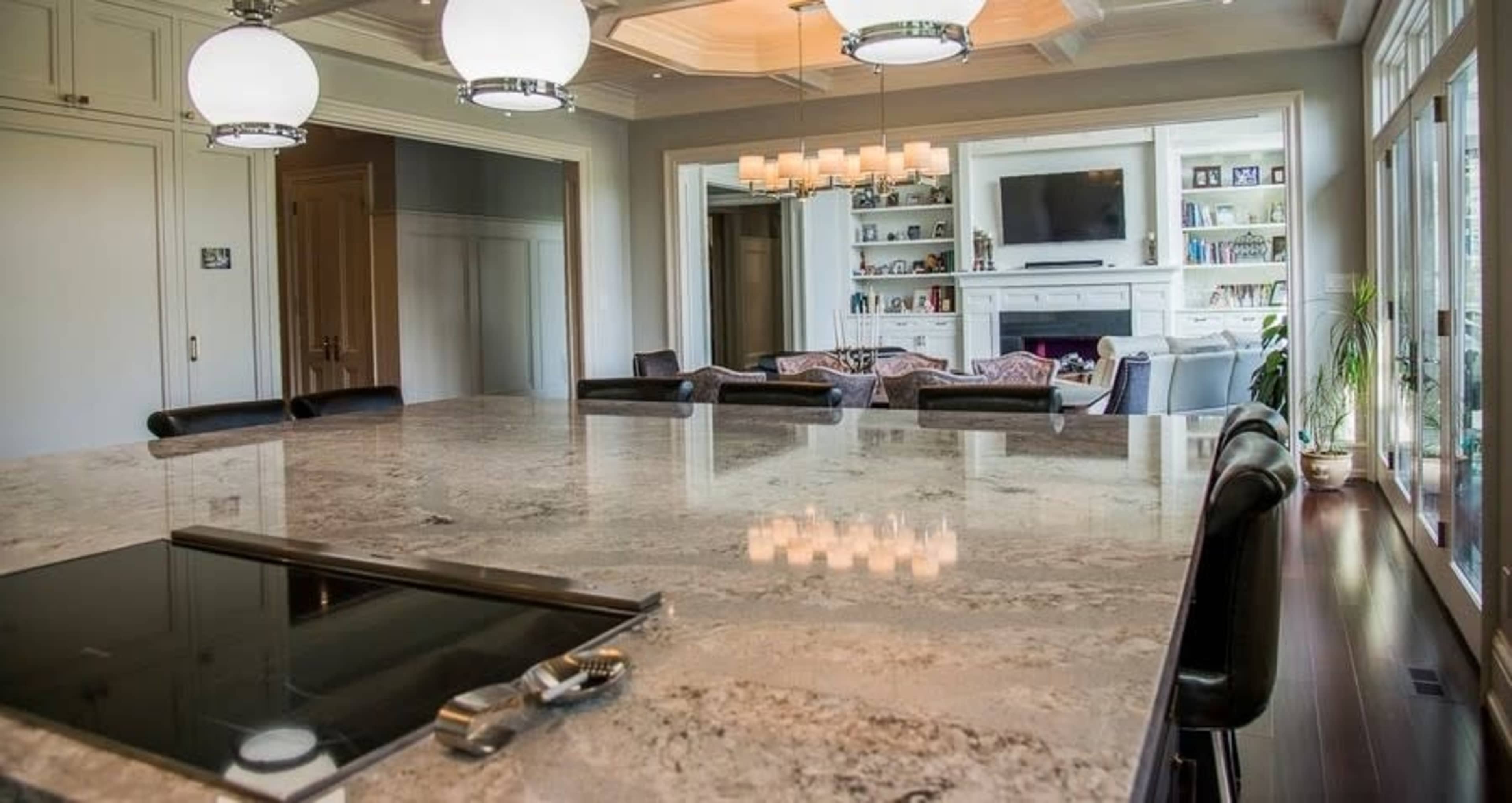 A spacious kitchen features a large granite countertop with a stovetop, and a living area with a television and bookshelves is visible in the background.