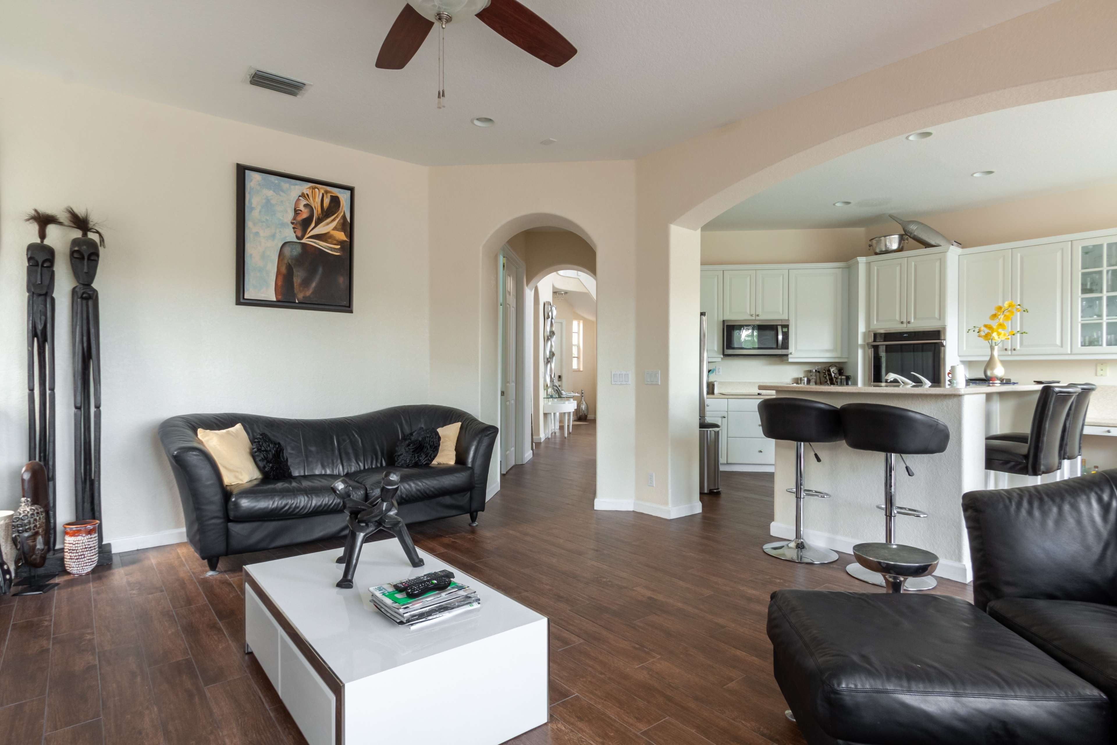 A modern living room with a black leather sofa, a white coffee table, and an open kitchen area visible in the background.
