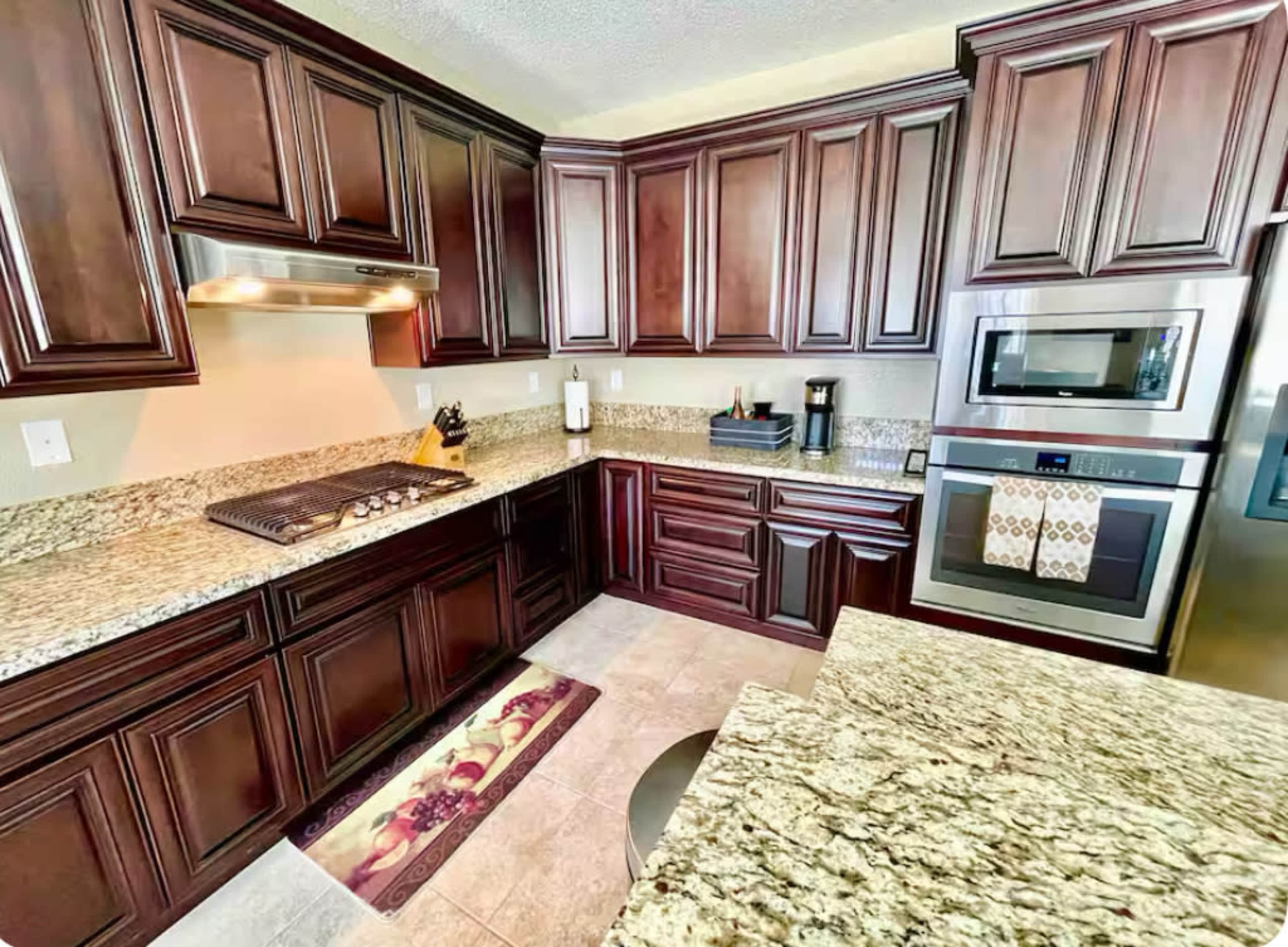 The kitchen features dark wood cabinets, granite countertops, a stainless steel stove and microwave, and a decorative rug on the floor.