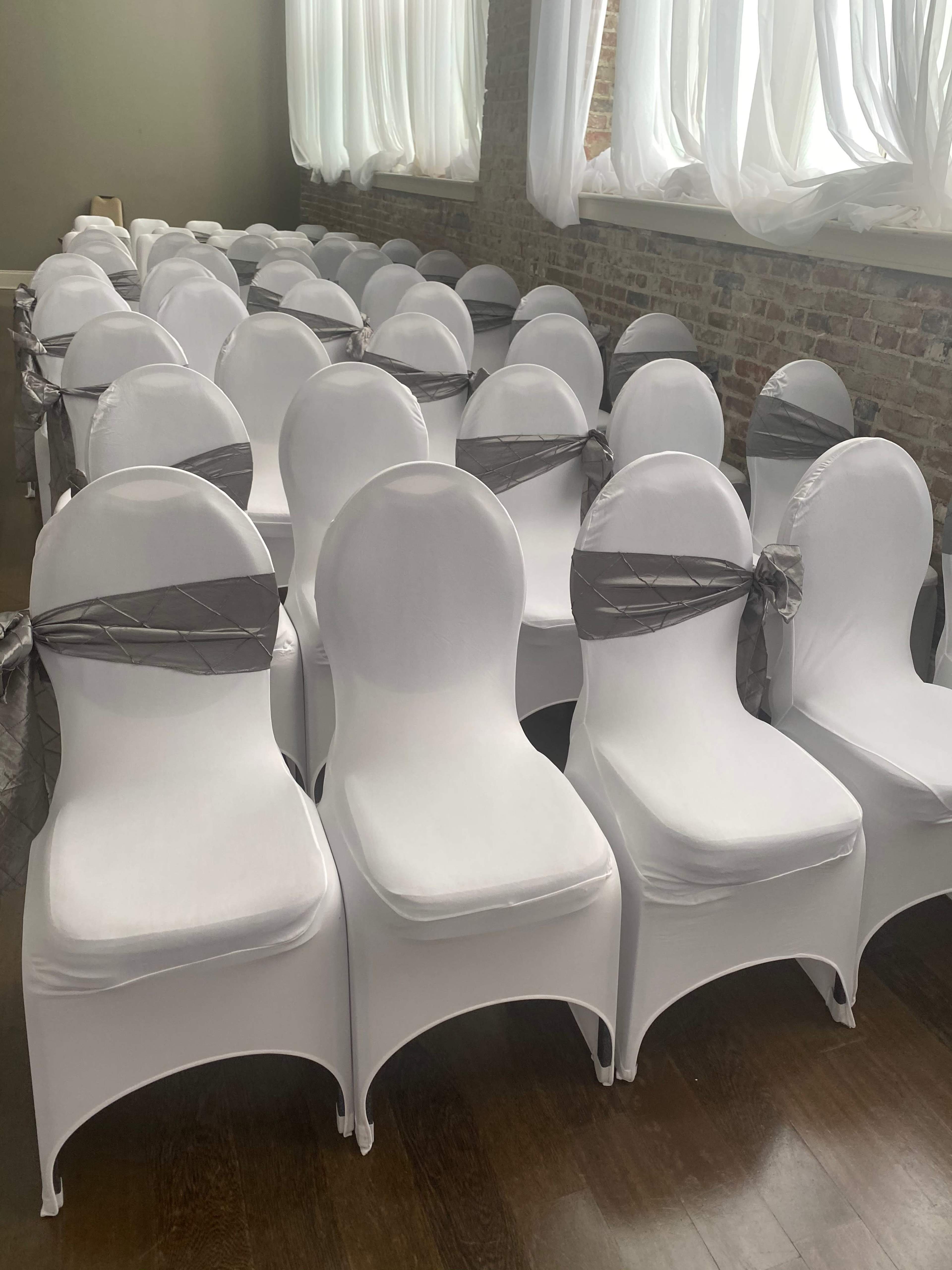 A large number of white chairs arranged neatly in a room, each adorned with a silver satin ribbon tied around the backrest.