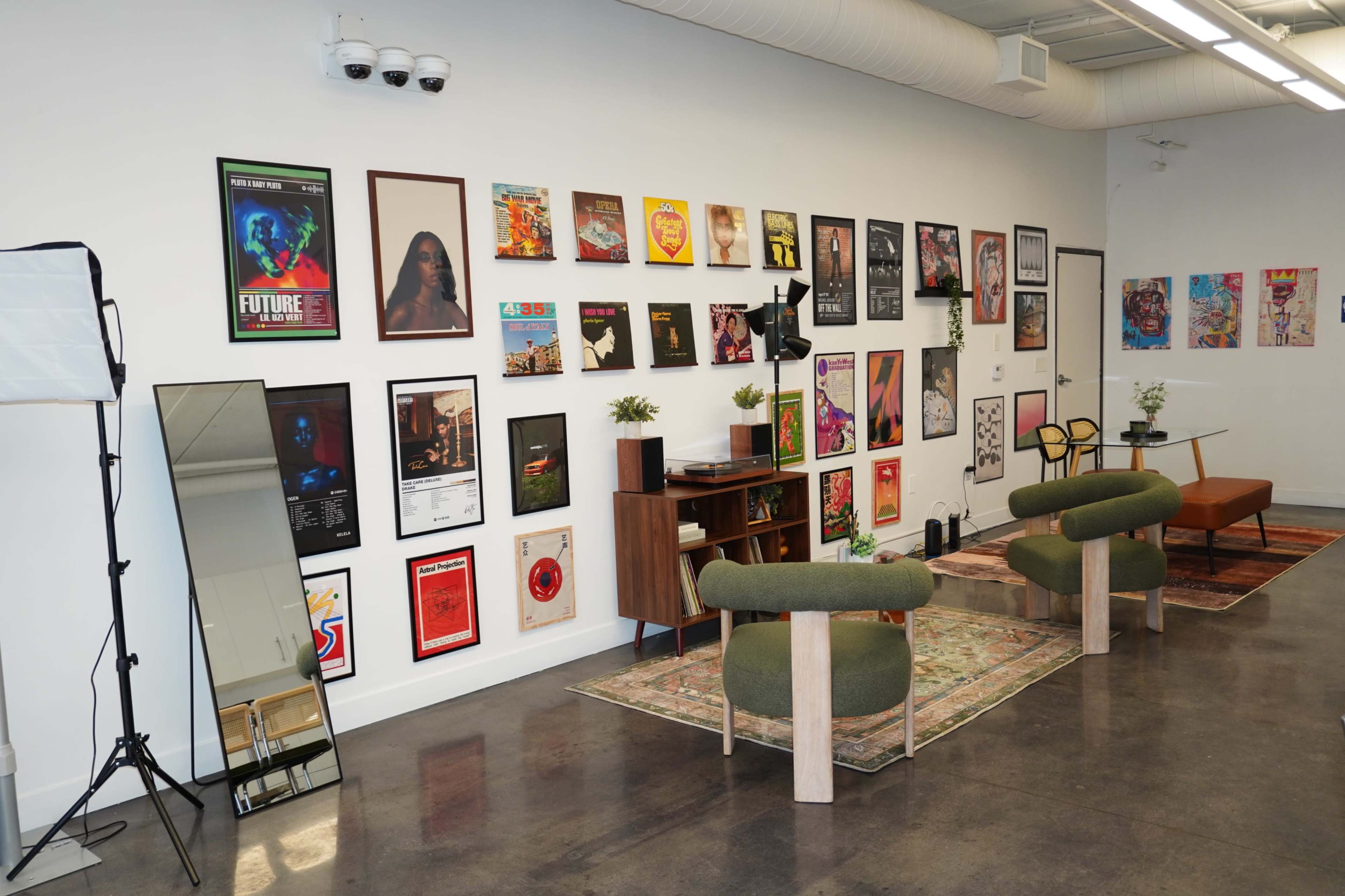 The image shows a modern room with art posters on the wall, two green chairs, a coffee table, and a decorative rug on a polished concrete floor.