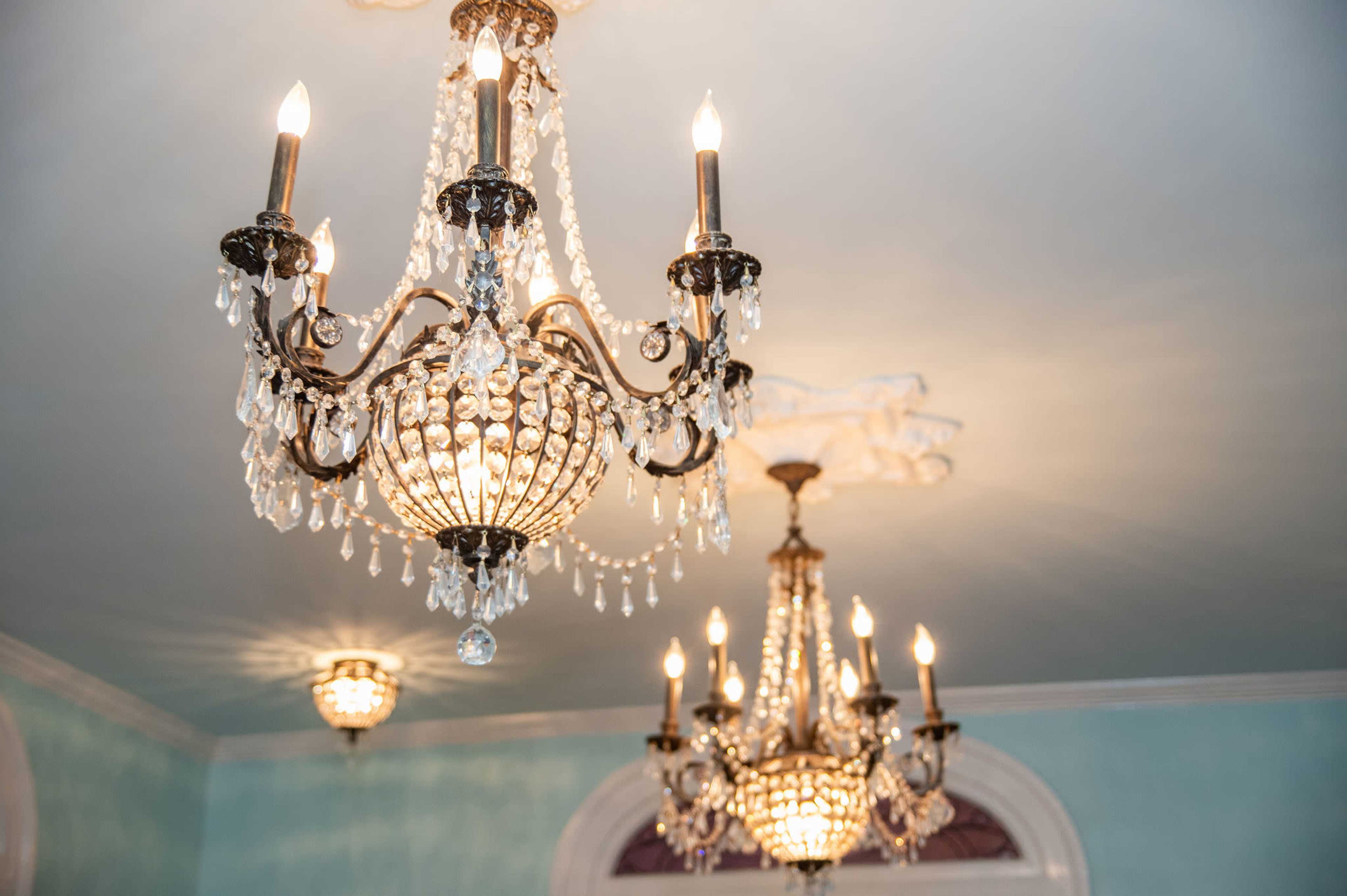 Two ornate chandeliers with crystal accents hanging from a ceiling, illuminating a softly colored room.
