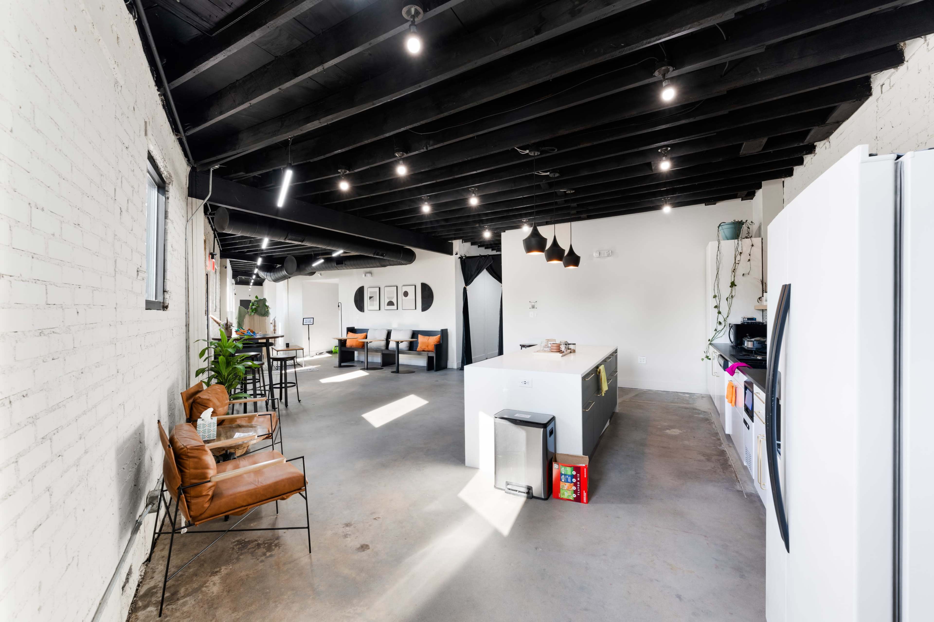 The image shows a modern, open-concept kitchen and living area featuring a central island, dining space, and seating arrangements with orange chairs.