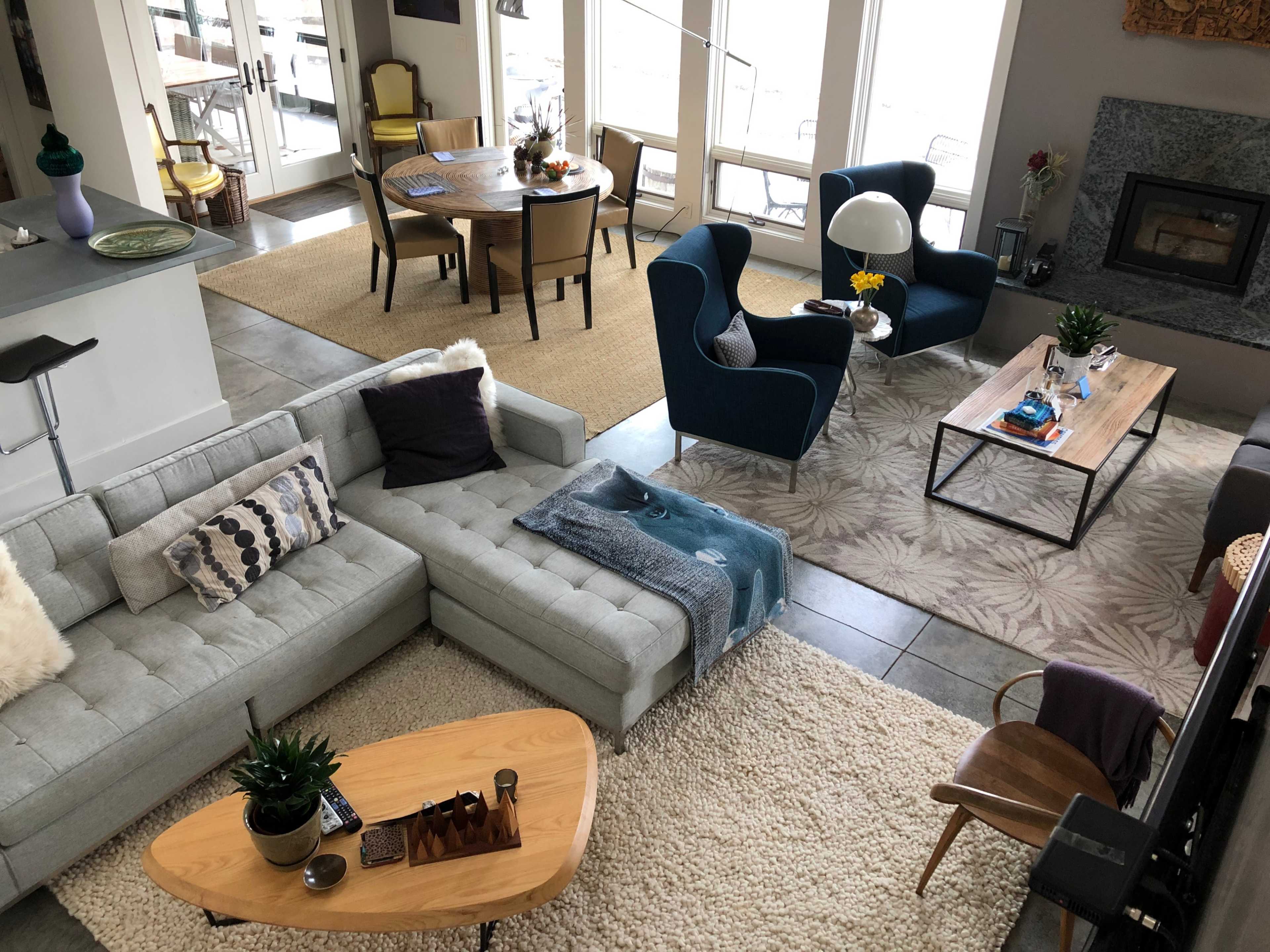 A modern living room and dining area with a gray sectional sofa, a blue armchair, a wooden coffee table, and a dining table set for several people.