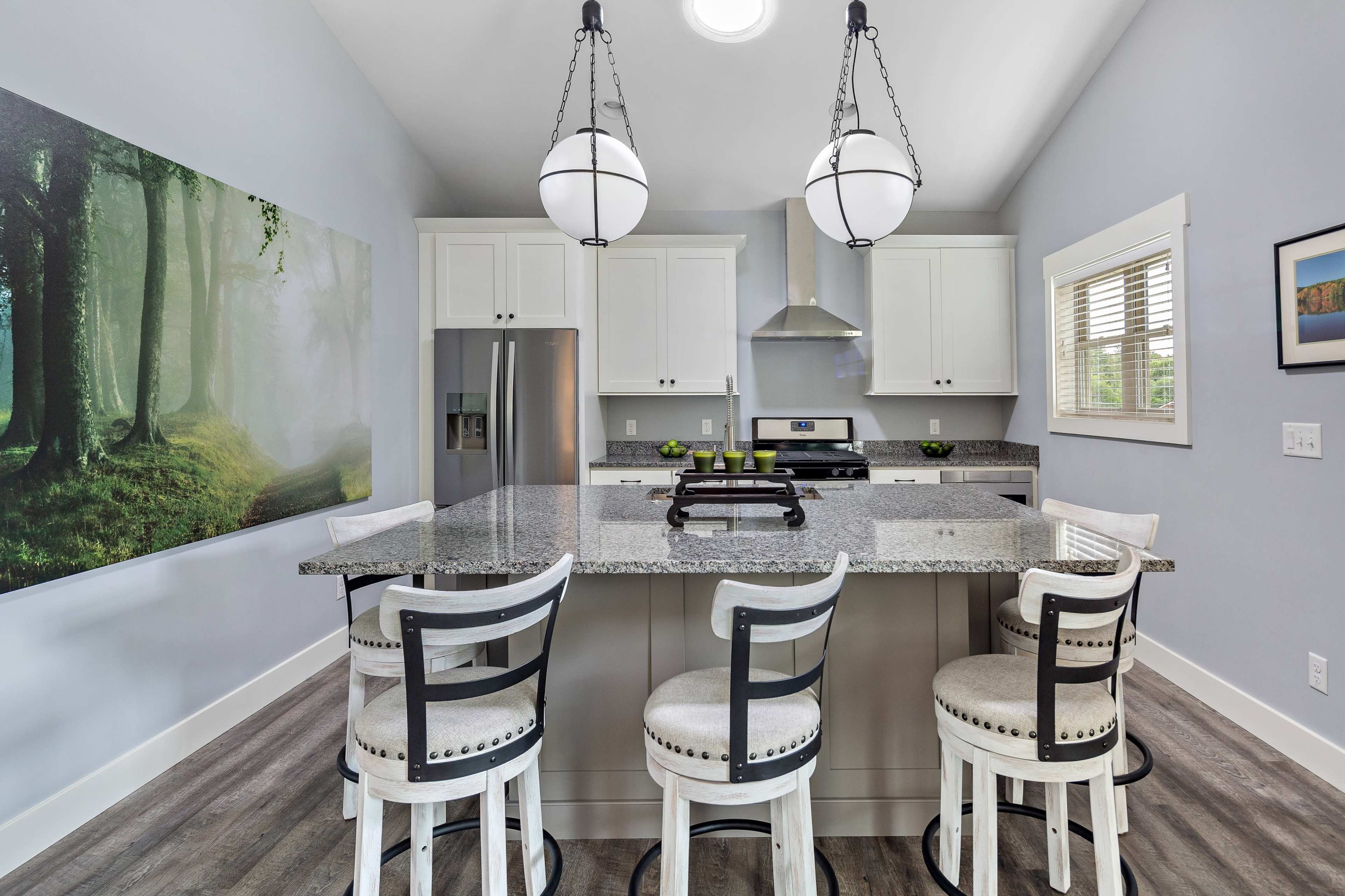 A modern kitchen features a central island with bar stools, sleek cabinetry, stainless steel appliances, and a large wall mural of a forest.