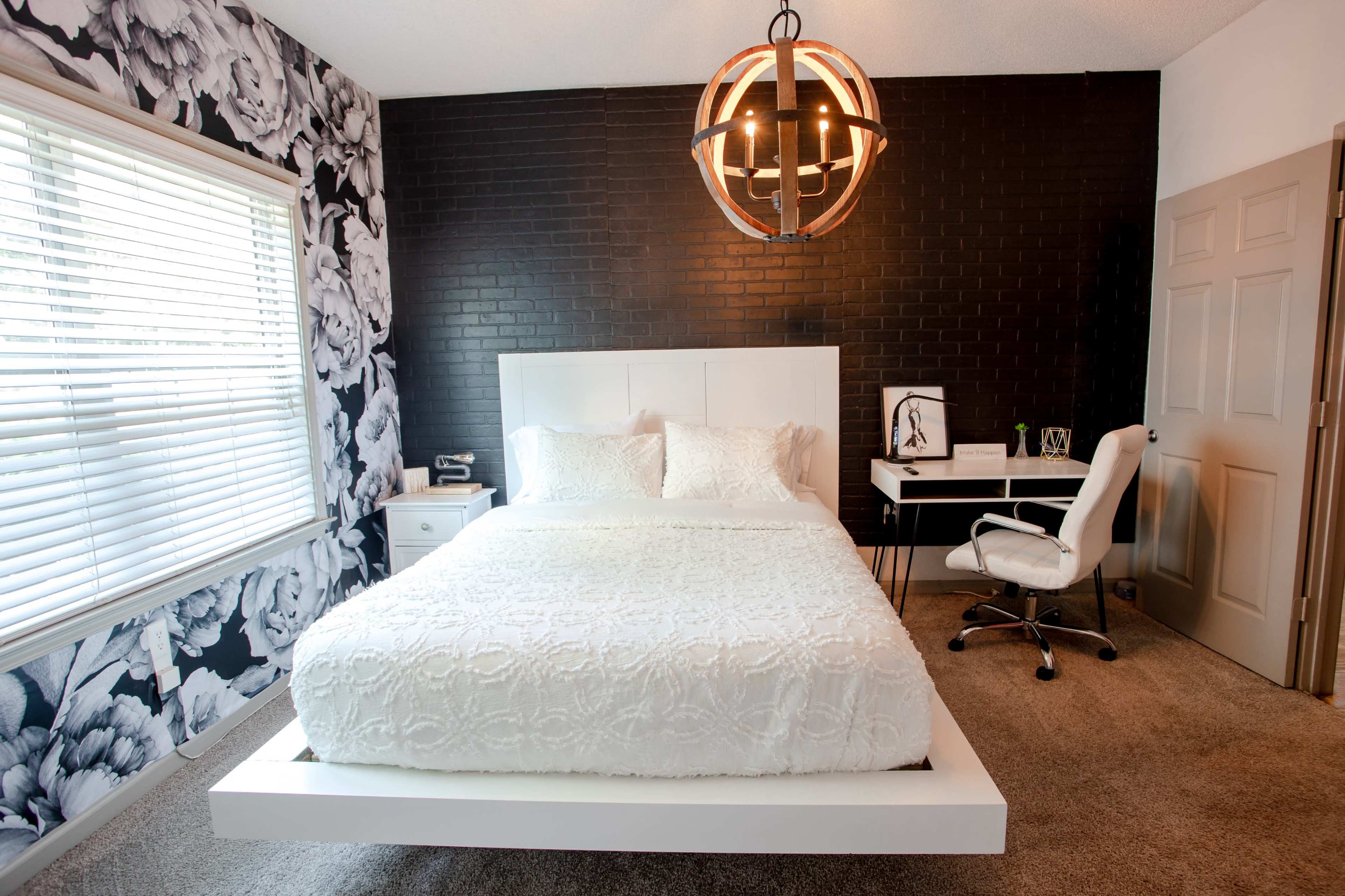 A modern bedroom featuring a white bed with a textured comforter, a desk and chair, and a black and white floral accent wall.