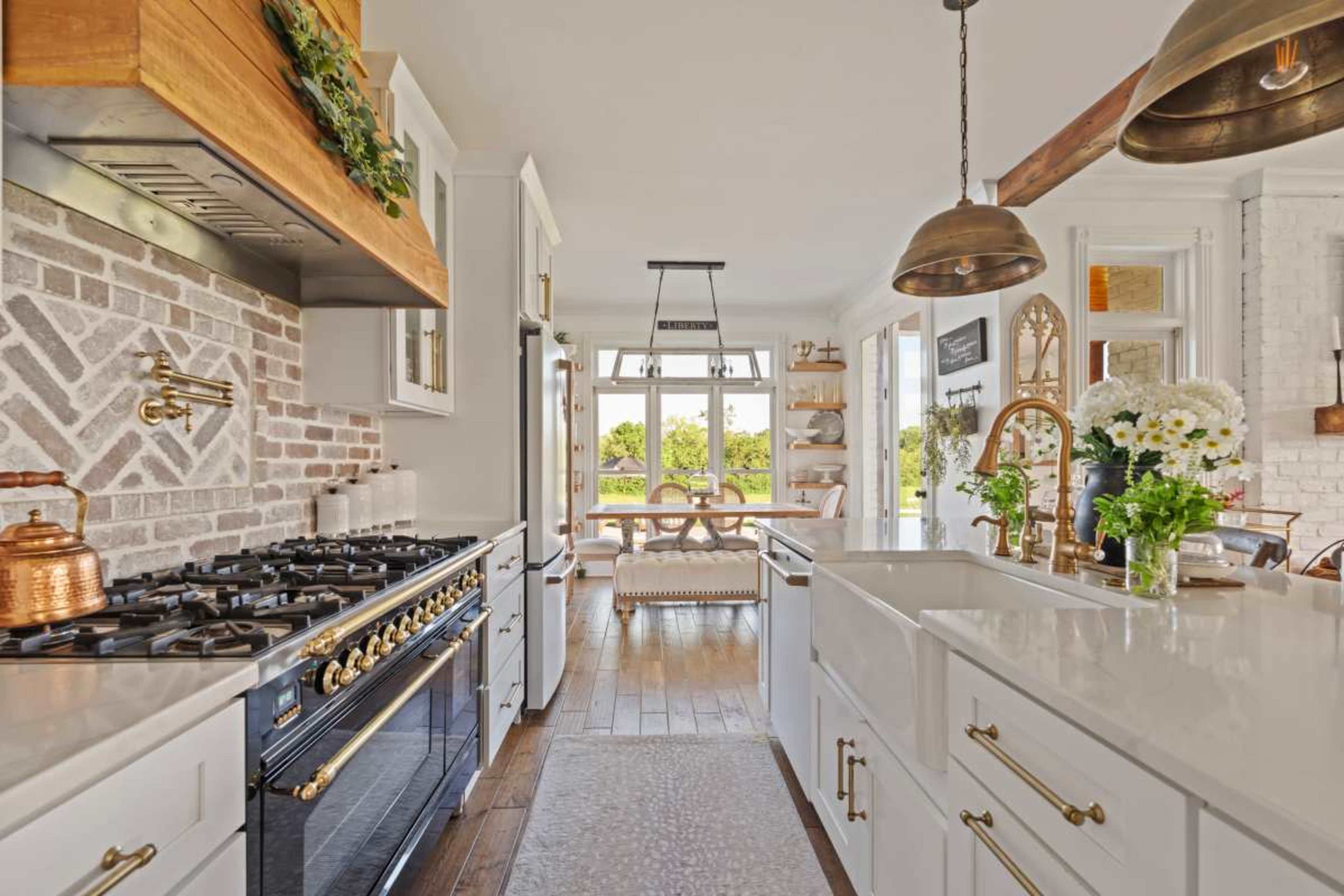 The image shows a modern kitchen with a gas stove, white cabinetry, and large windows overlooking a dining area.