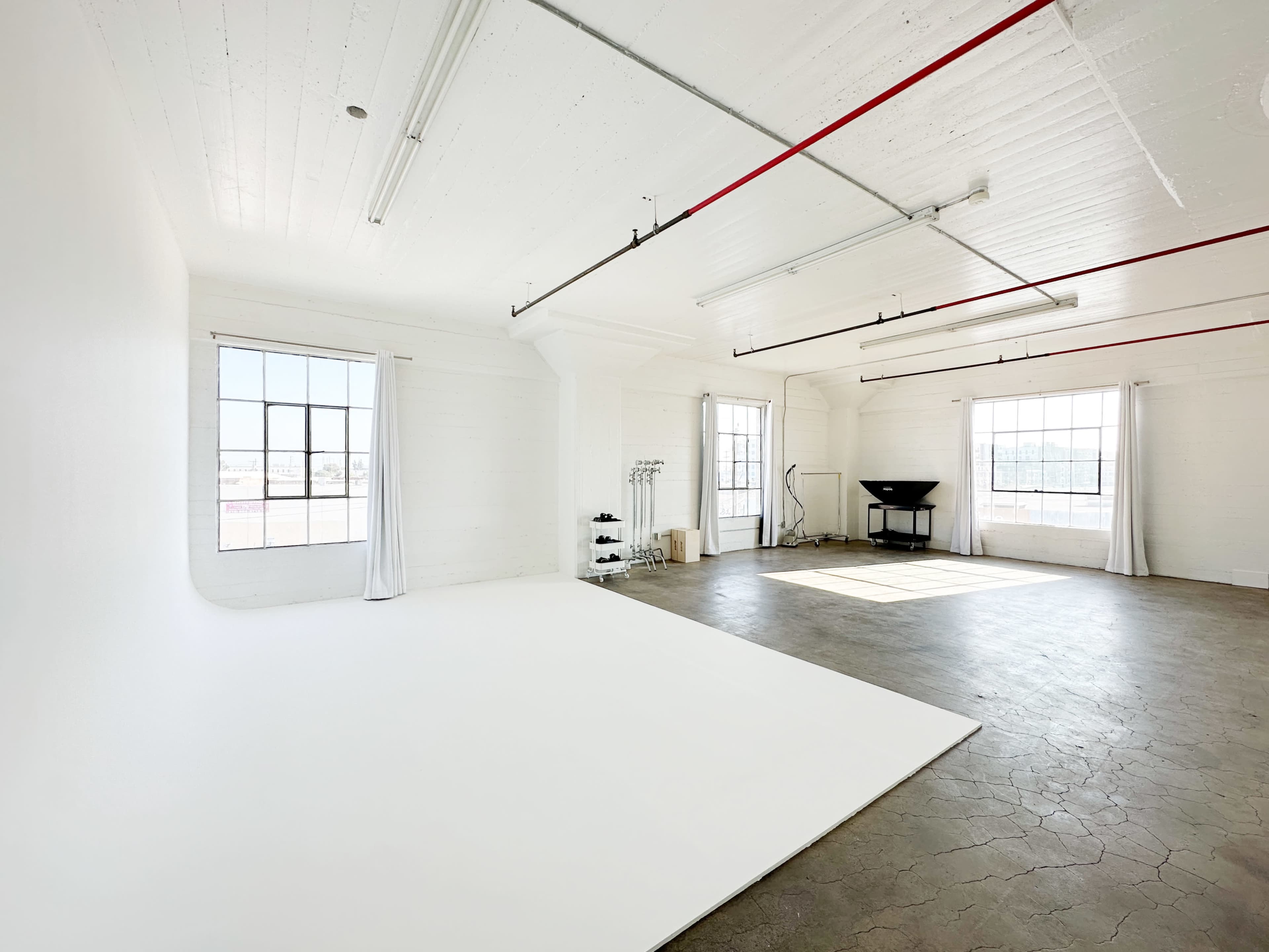 A bright, spacious studio with white walls, large windows, and a clean, empty area for photography or staging.
