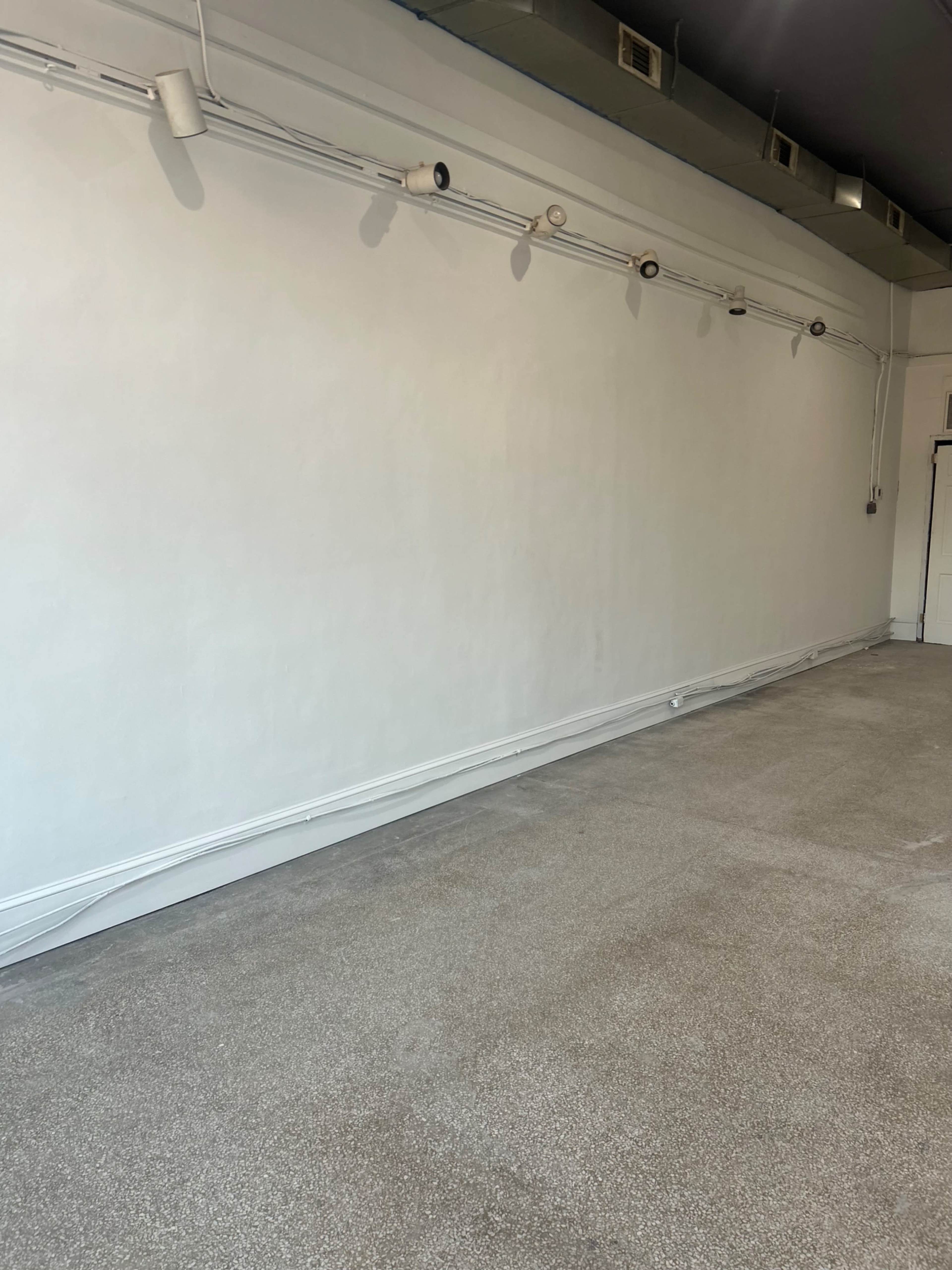 The image shows a blank, empty room with a white wall and a carpeted floor.