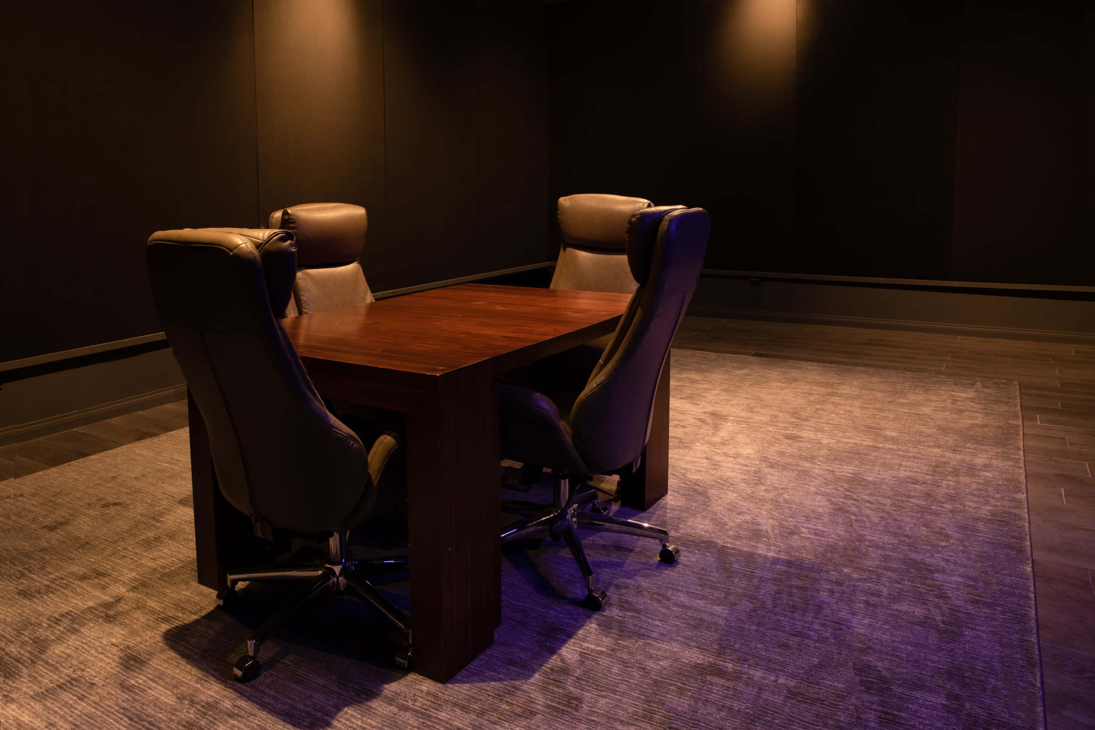 A dark room features a wooden table surrounded by four swivel chairs.