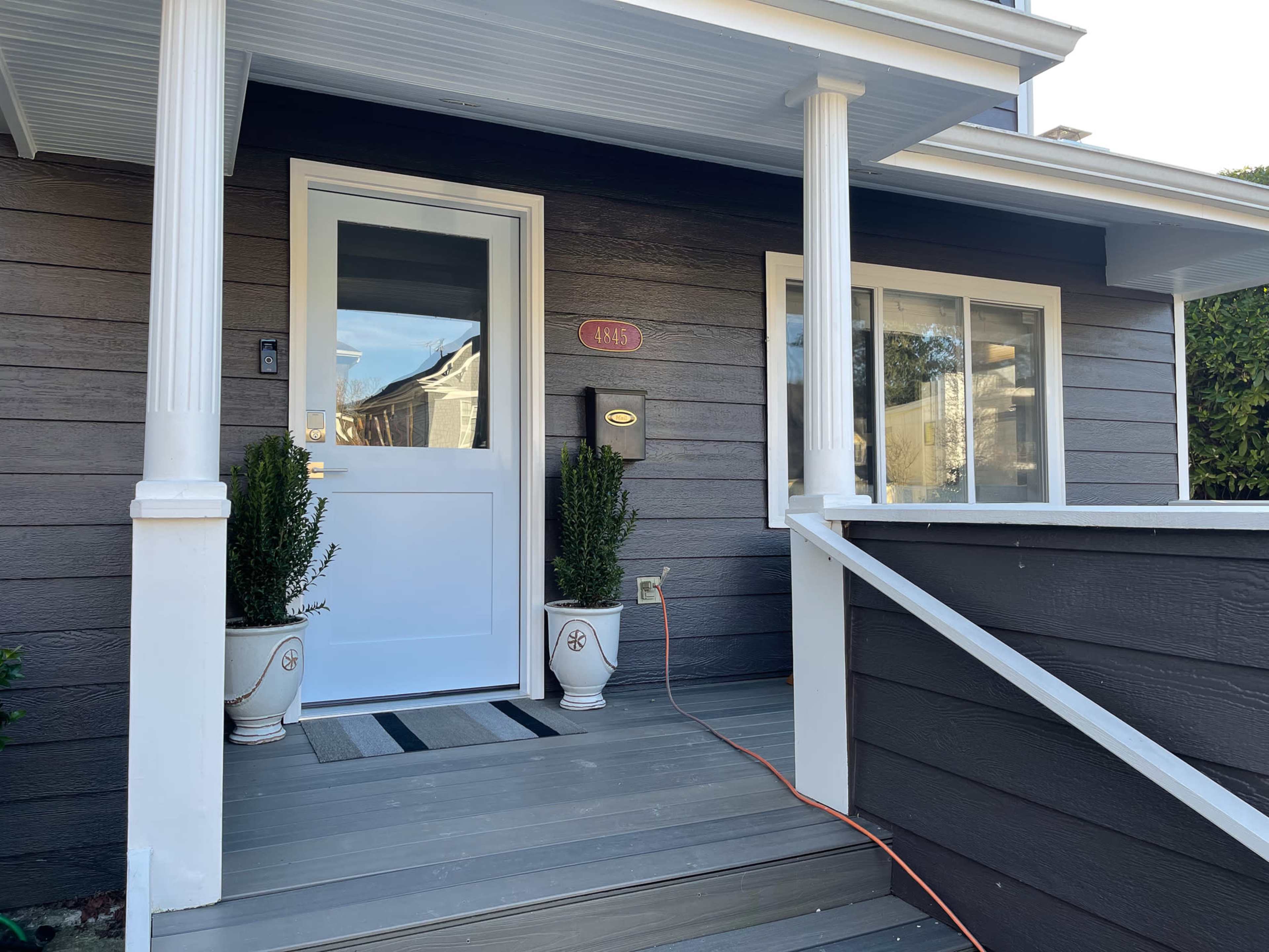 The entrance of a house featuring a white front door, symmetrical planters on either side, and a wooden porch with a sloped ramp.