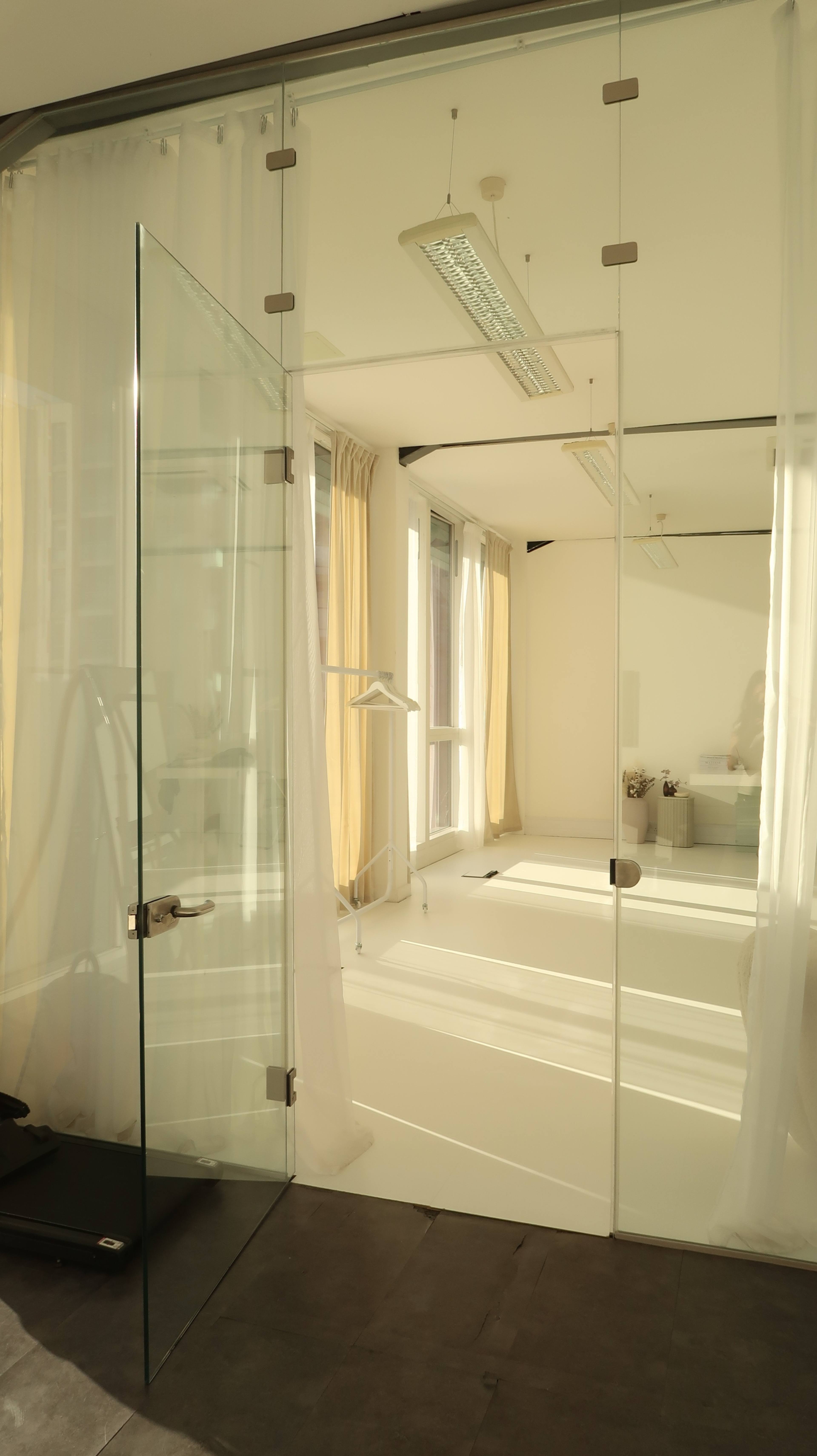 The image shows a bright room with large glass doors, sheer curtains, and minimal furnishings.