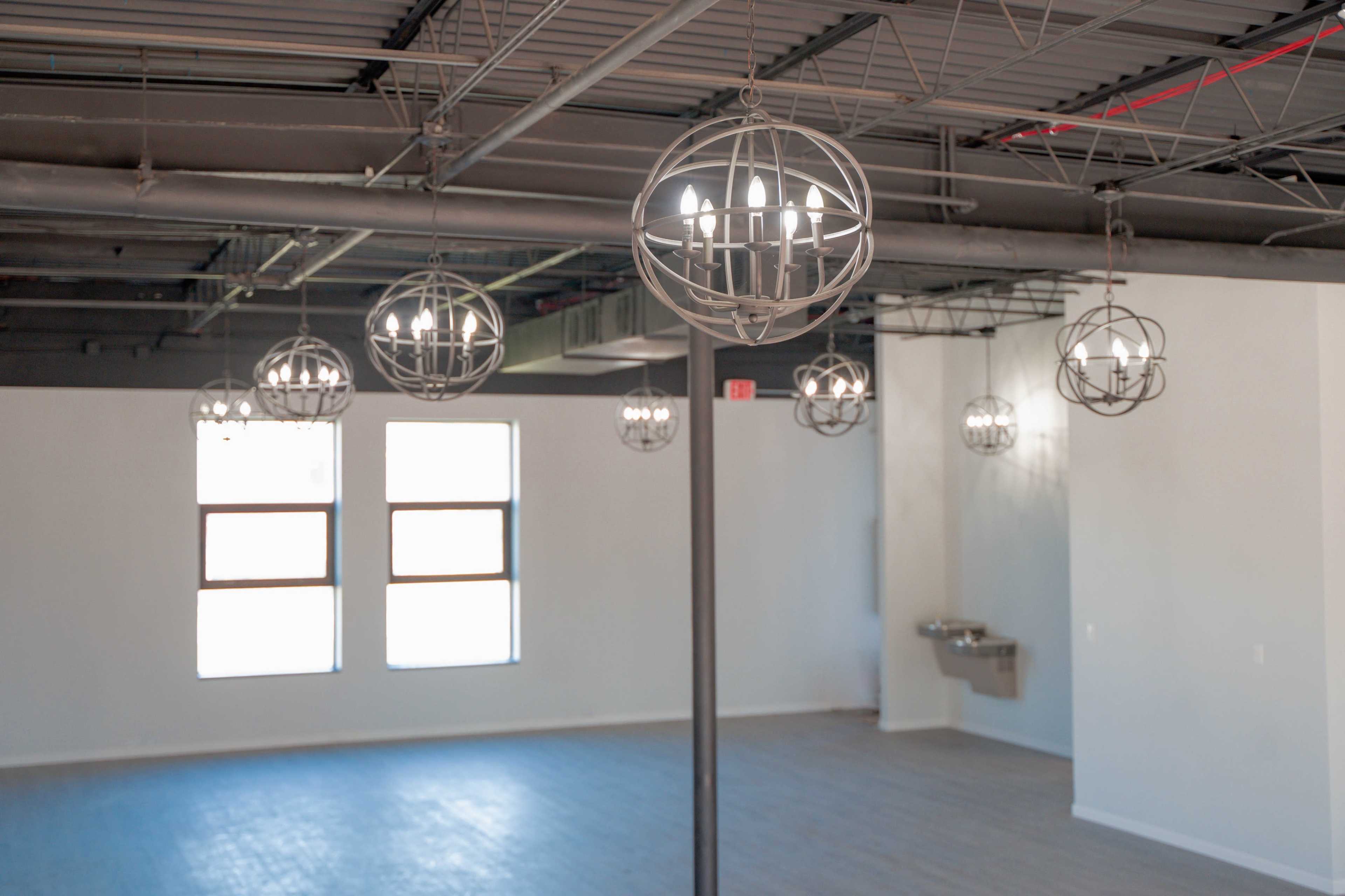A spacious, empty room with several round pendant lights hanging from the ceiling and large windows along one wall.