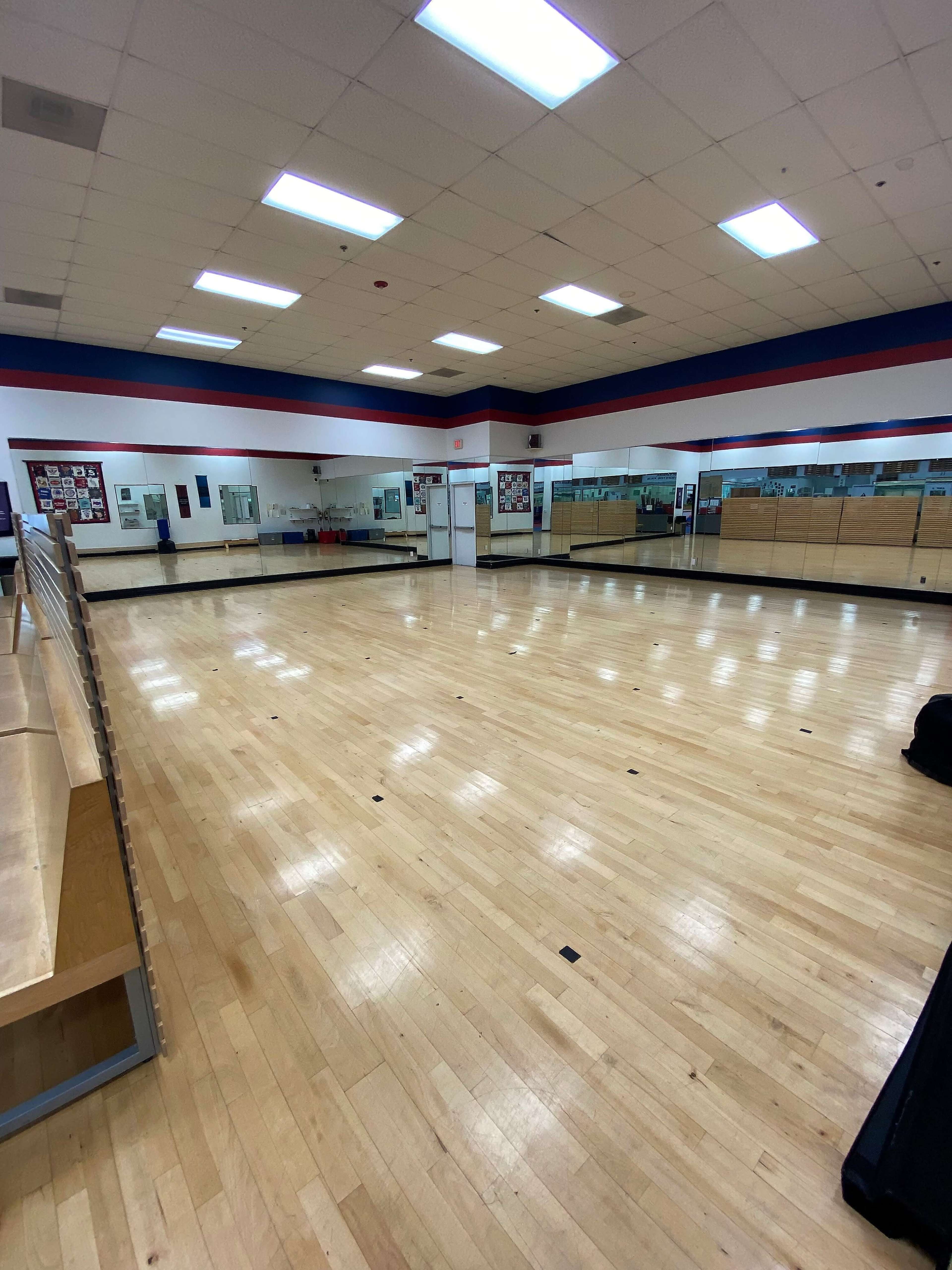 A spacious, well-lit dance studio featuring hardwood flooring and mirrored walls.