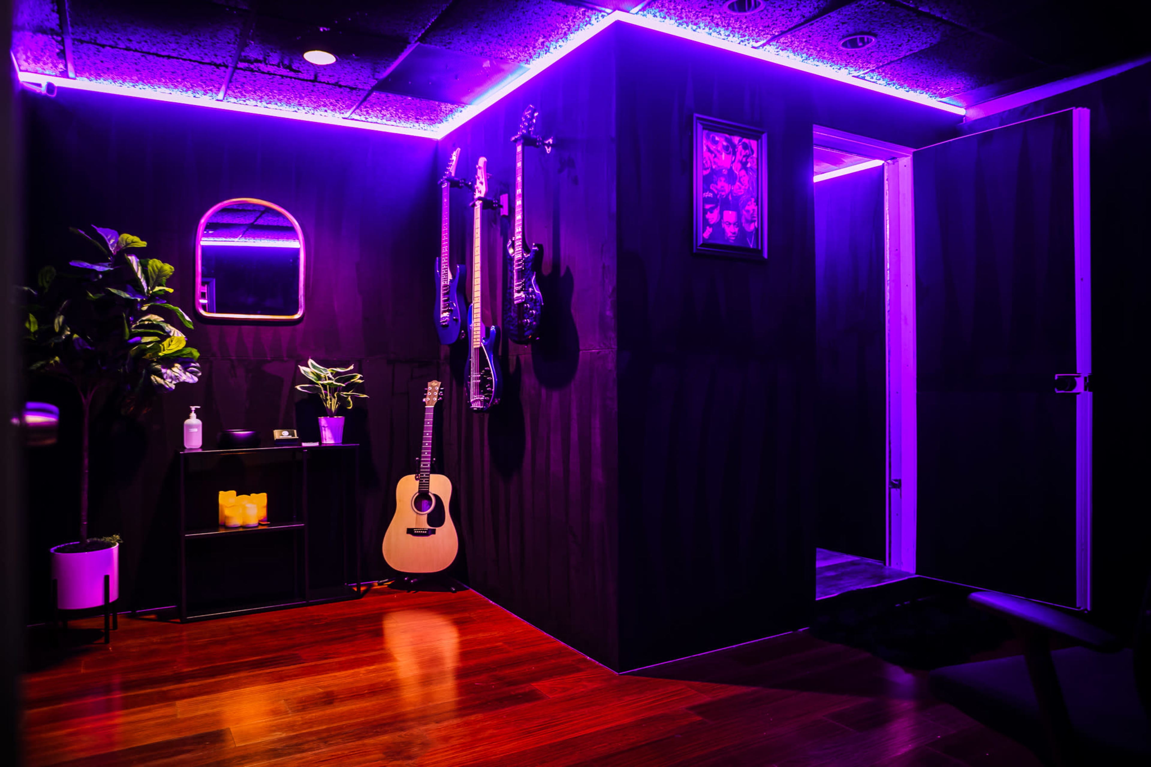 The image shows a dimly lit room with purple LED lights, featuring hanging guitars on the wall, a wooden floor, and a door leading to another space.