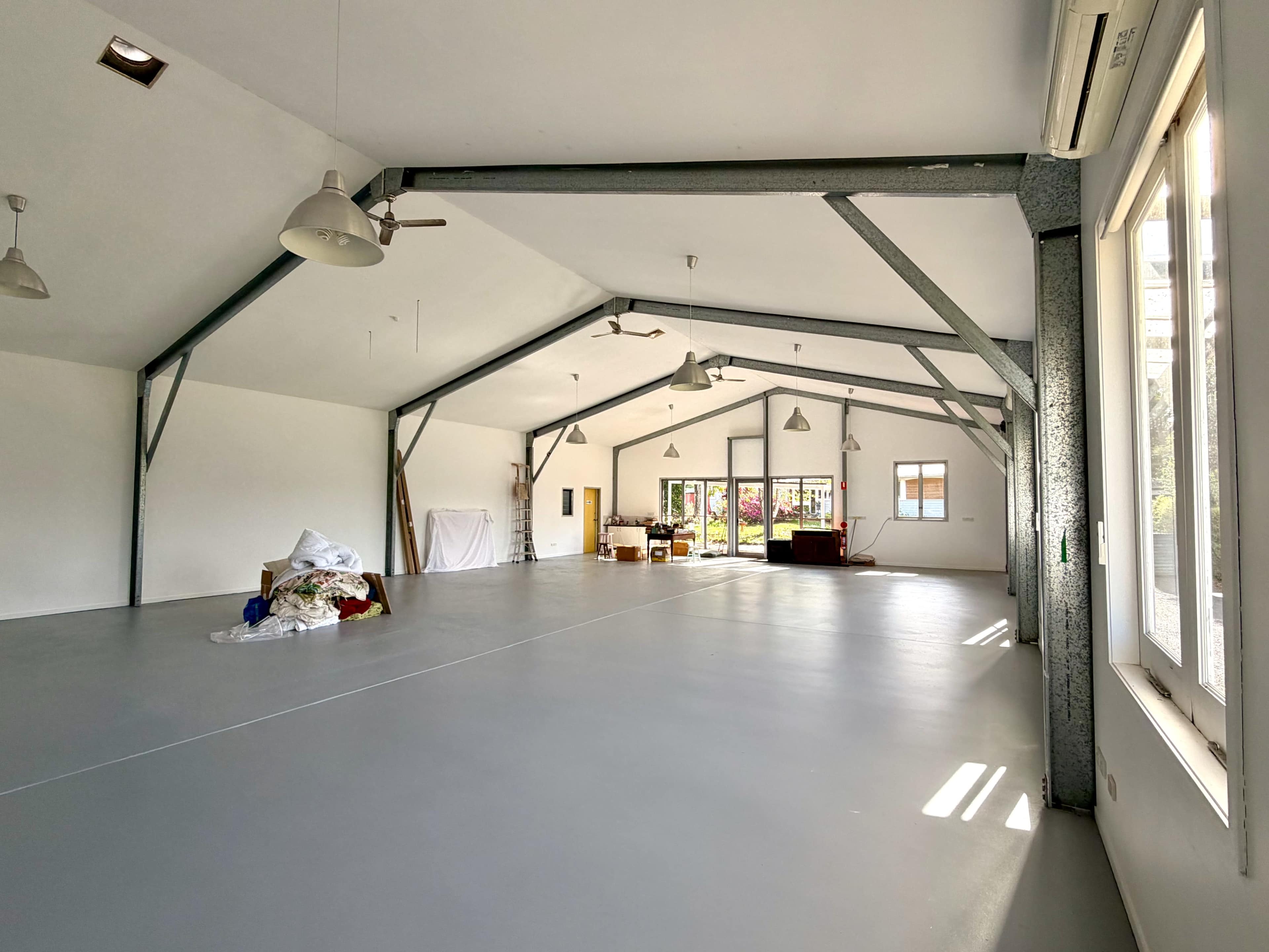 The image shows a spacious, empty room with high ceilings, large windows, and a smooth, gray floor.