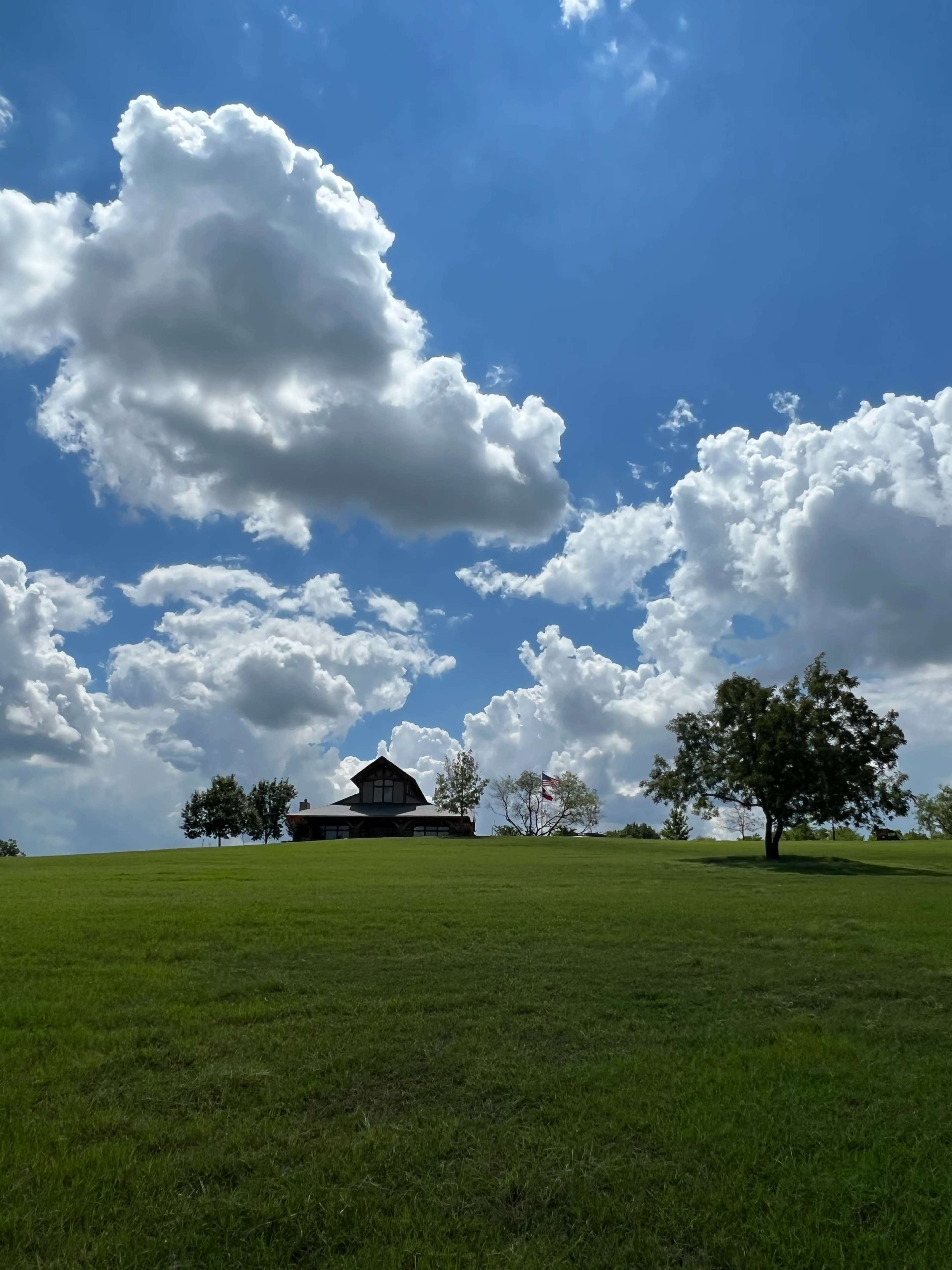 A house sits on a grassy hill beneath a sky filled with large, fluffy clouds.