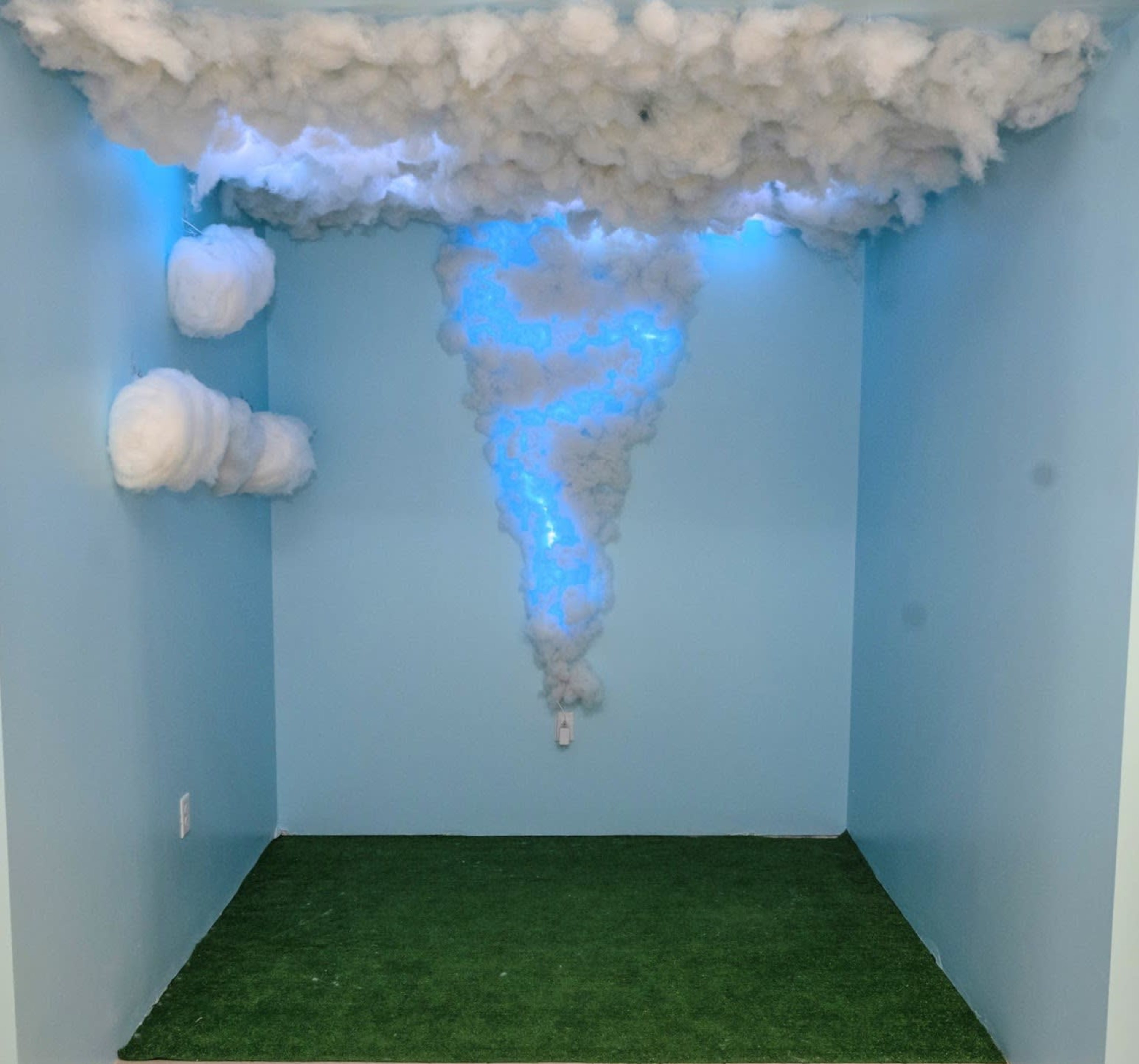 A small room with a blue wall and ceiling designed to resemble a storm, featuring artificial clouds and blue lights.