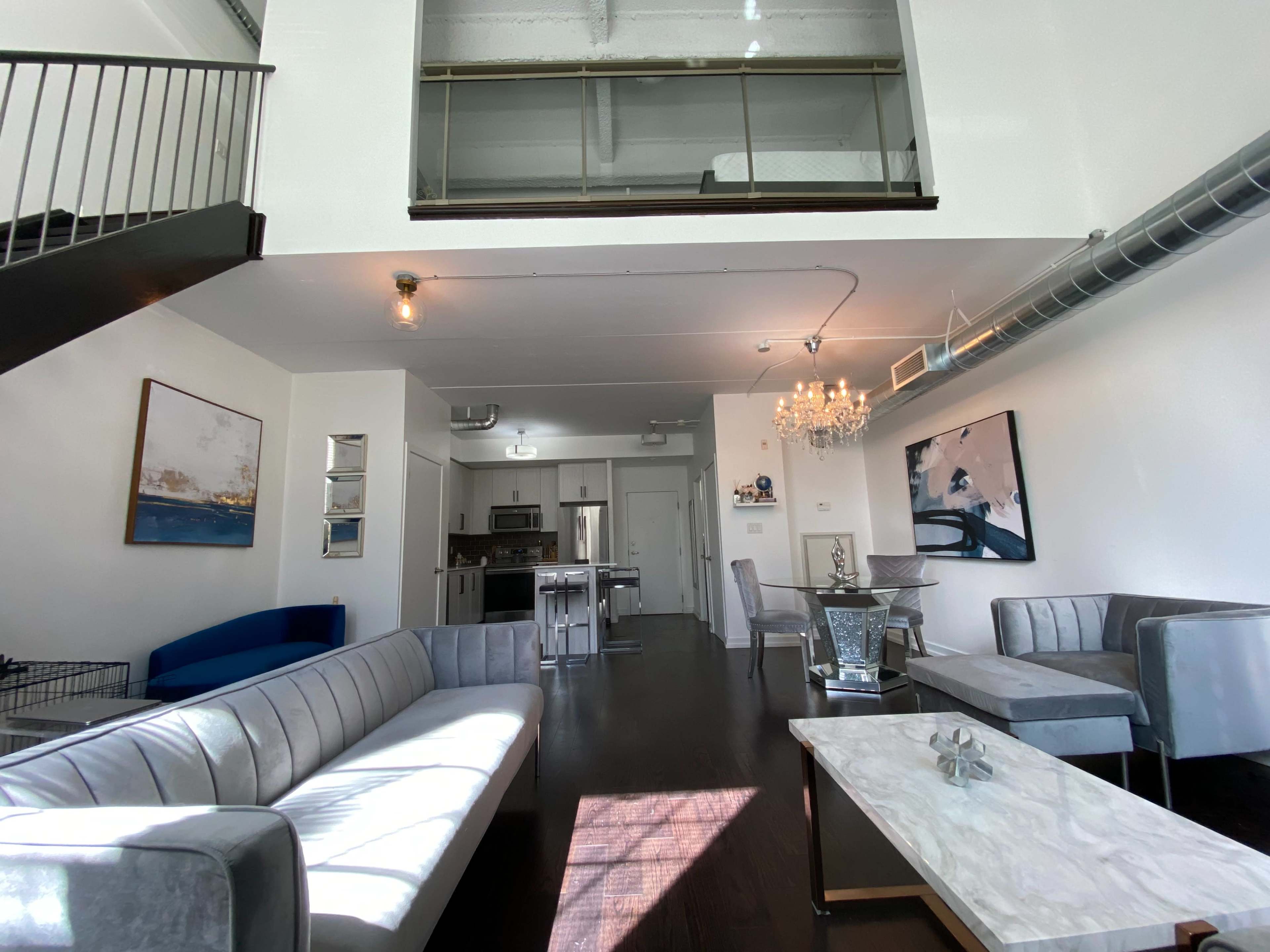 The image shows a modern, two-story living space with a dining area, kitchen, and a high ceiling featuring a chandelier.